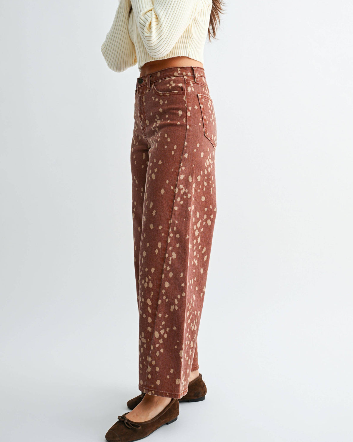 A woman modeling a cream ribbed turtleneck crop top and rust-brown wide-leg trousers with a small white floral pattern, paired with dark brown flat shoes, against a plain light gray studio background. Bambi Deer Print Seamed Slim Wide Leg Jeans | Blackbird Boutique