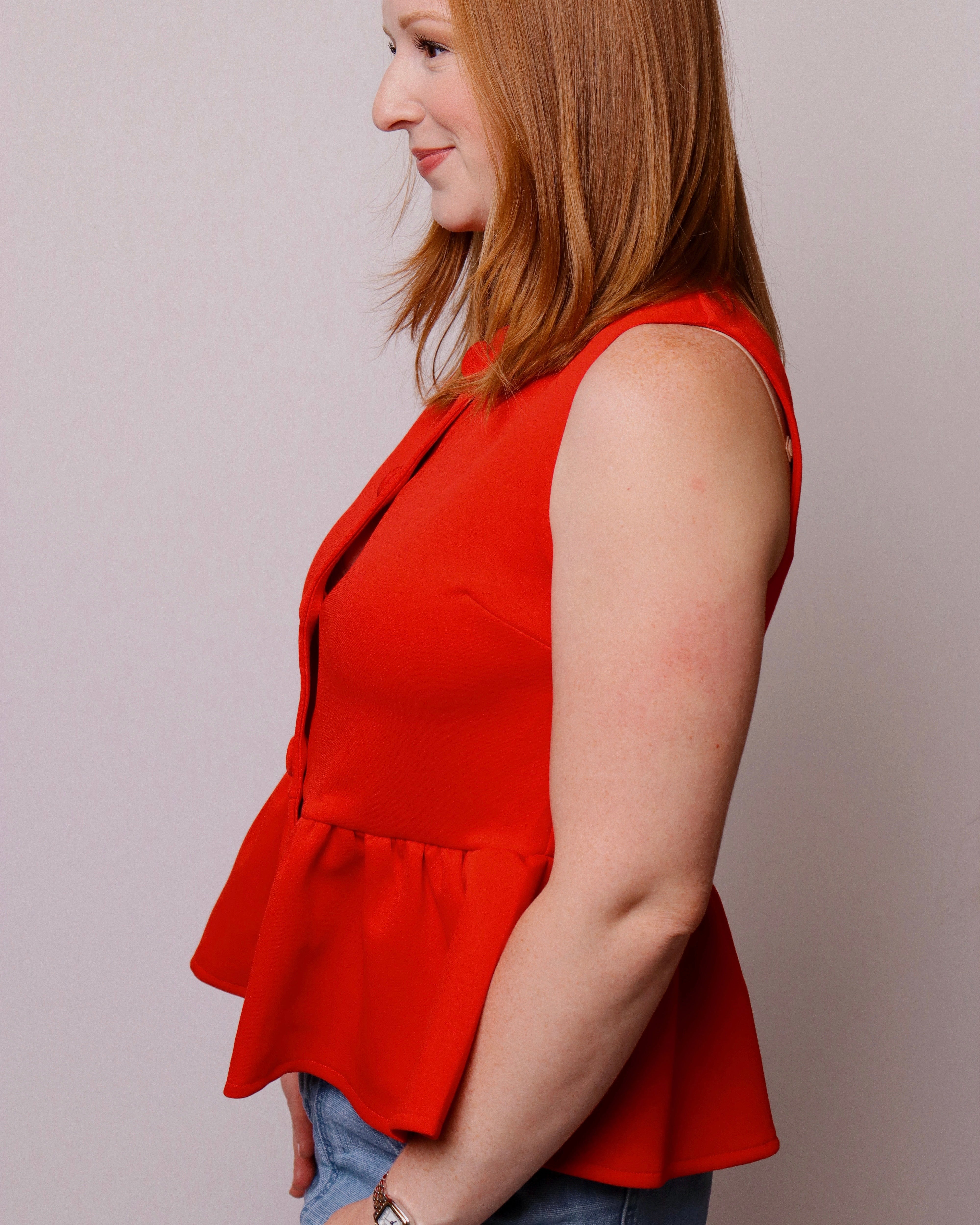 Woman wearing a red peplum top against a plain background