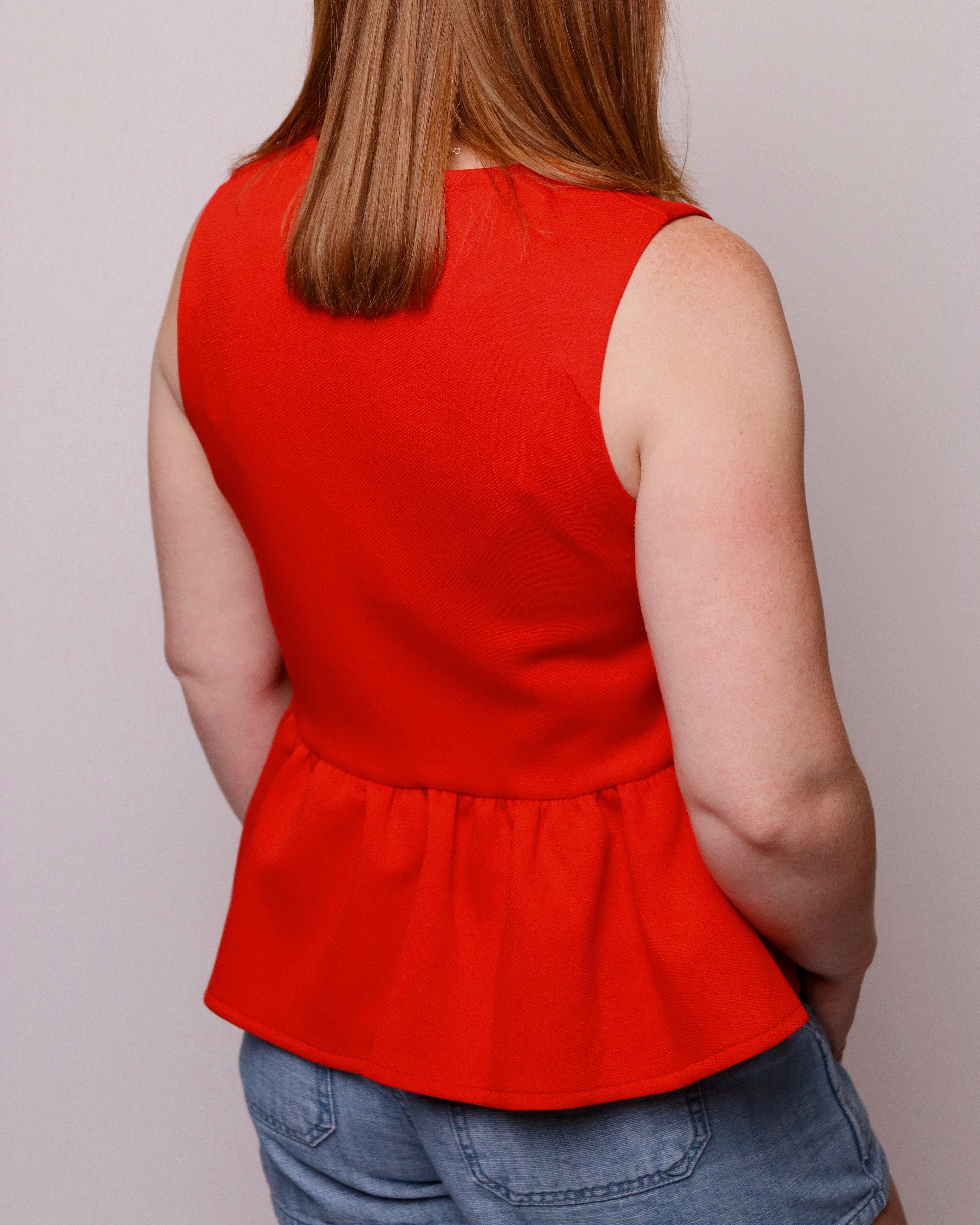 Person wearing a red sleeveless top and blue jeans against a plain background