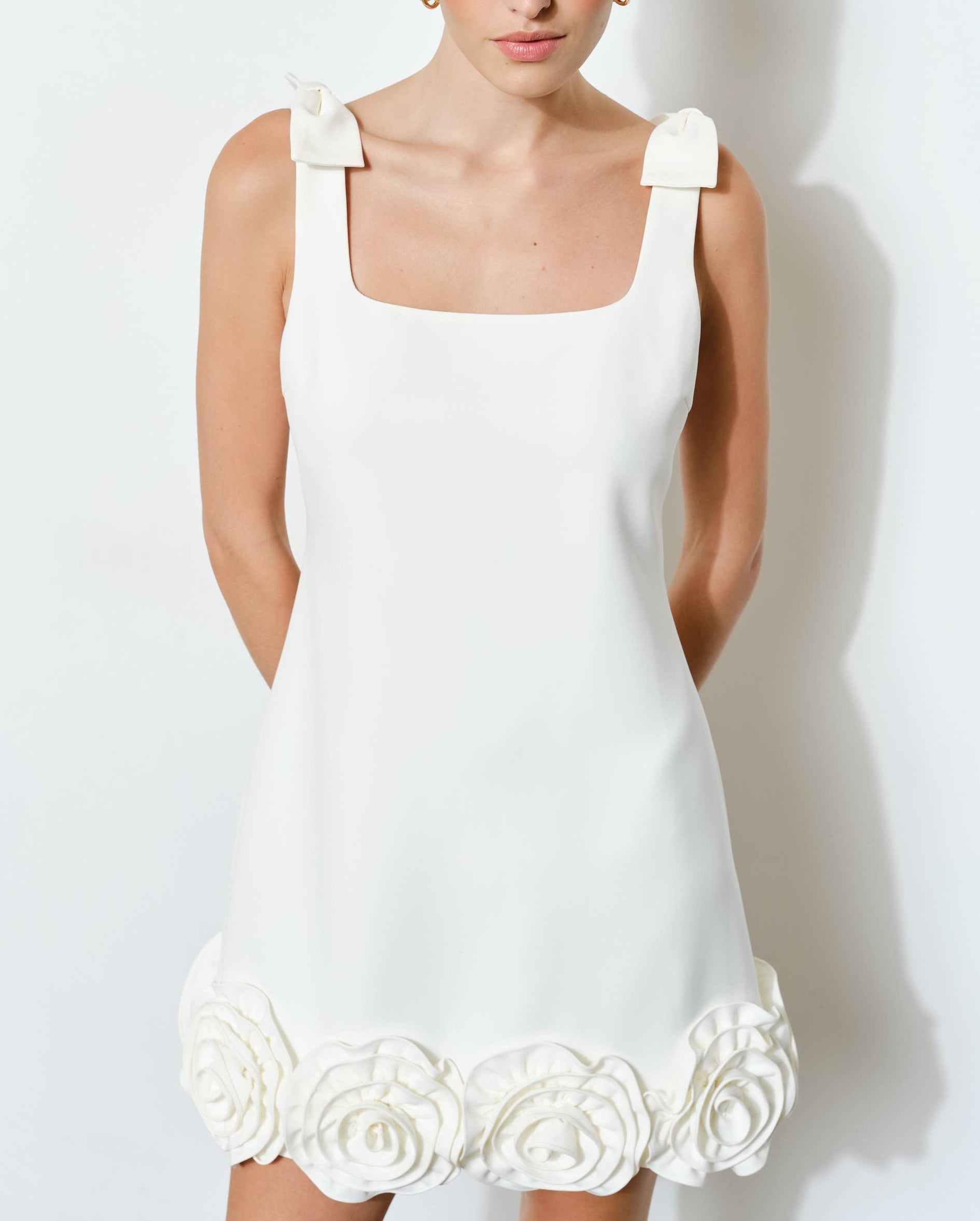 Woman wearing a white dress with floral details on a plain background