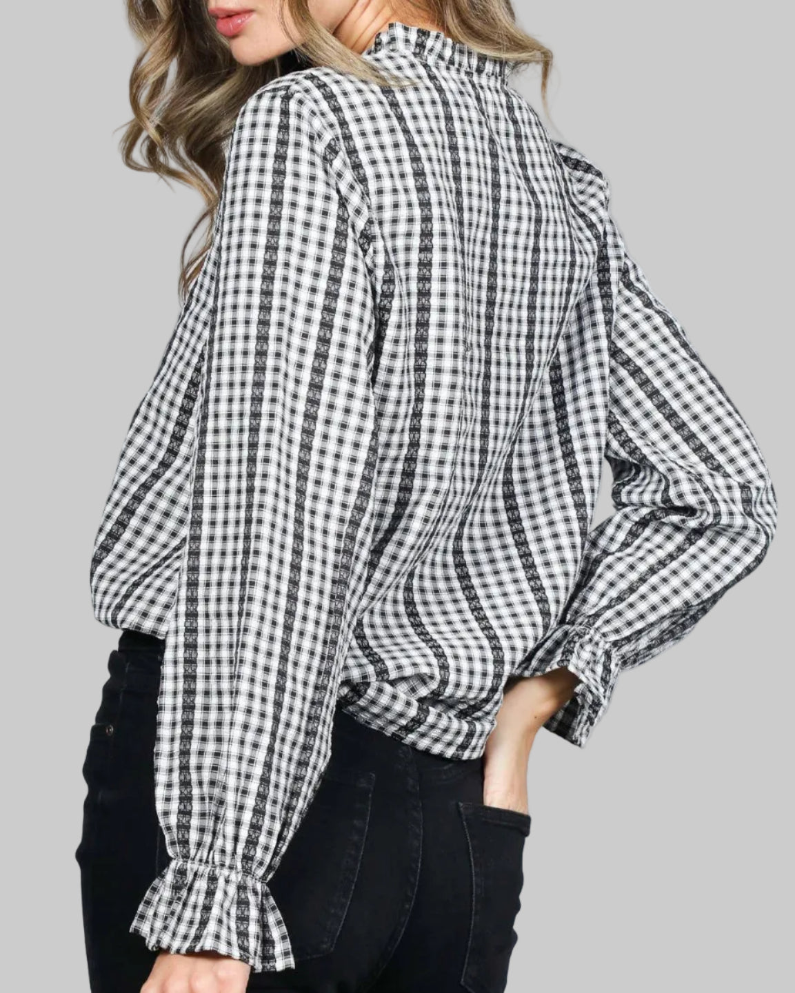 Model wearing a black and white gingham button up top. Ruffled neckline and elasticized long sleeves