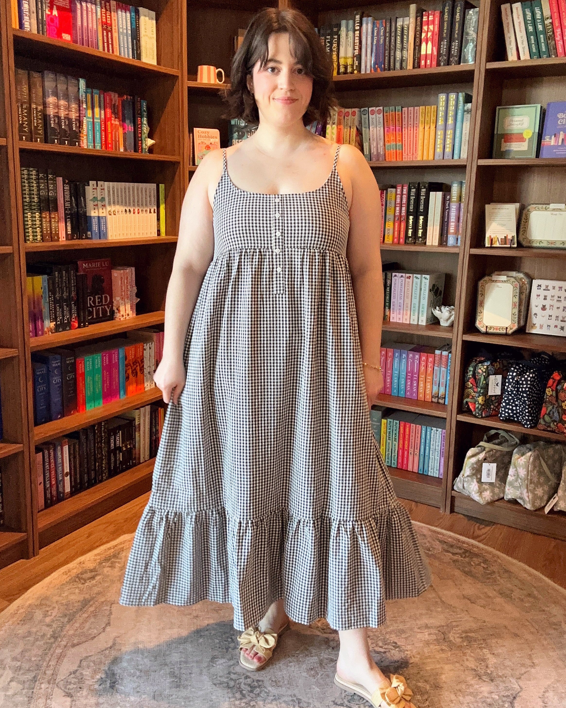 Woman in a checkered dress standing in front of a bookshelf filled with books.