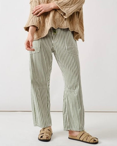 Person wearing a beige cable knit sweater and striped pants on a white background