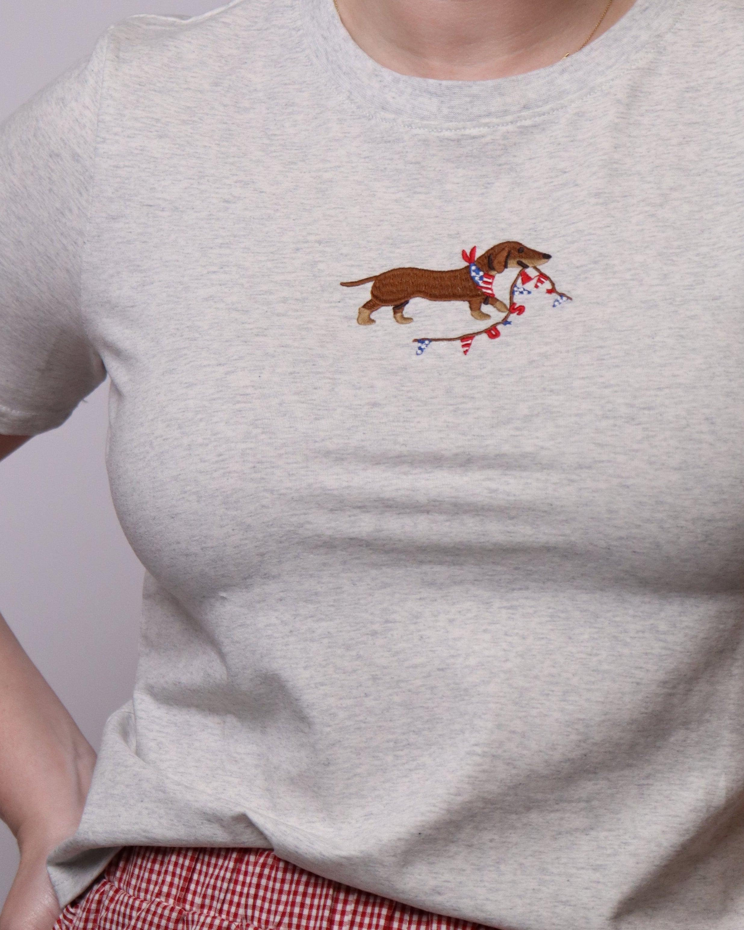 Woman wearing a light gray sweater with a dachshund design on a plain background