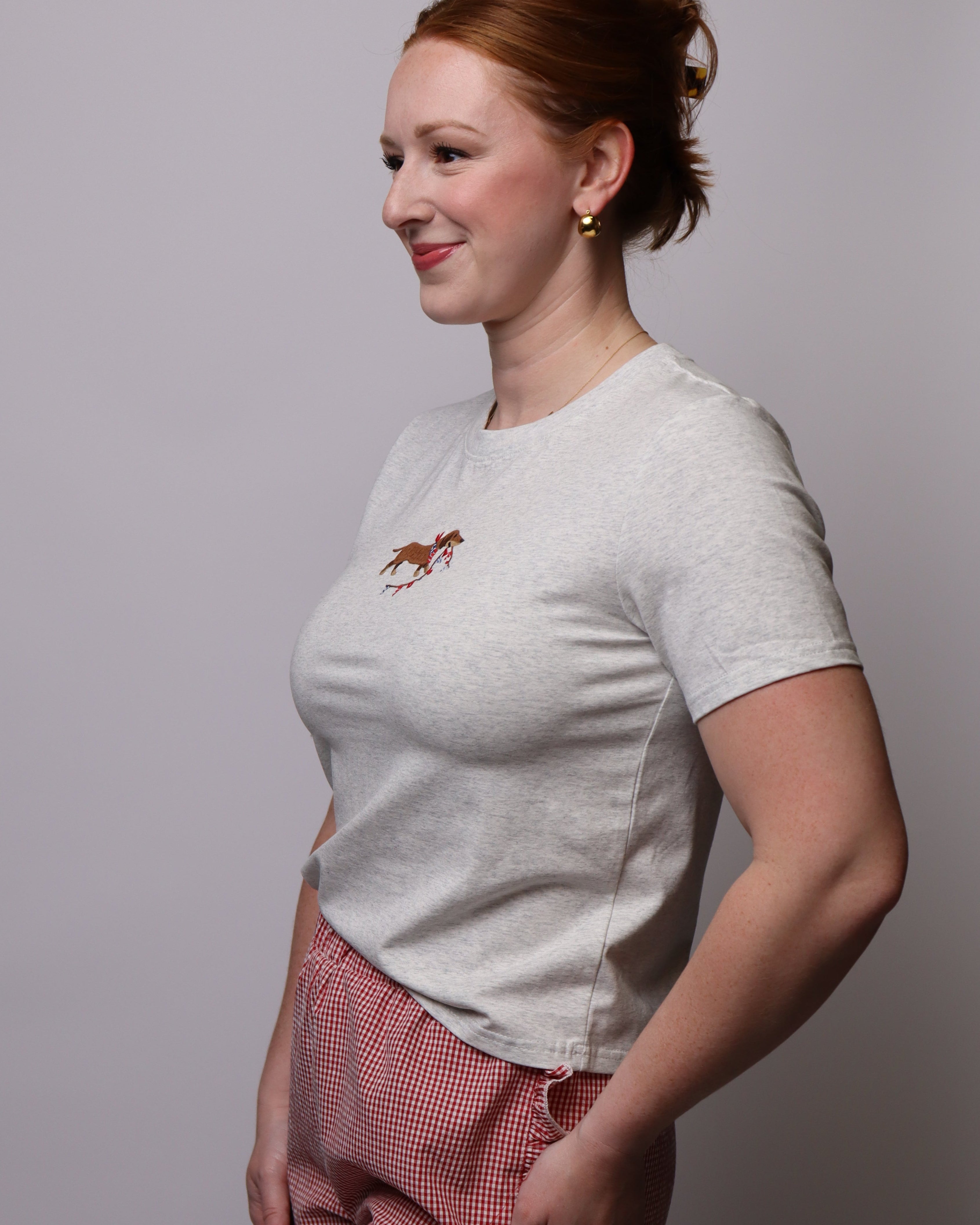 Woman wearing a Heather Gray t-shirt with a embroidered dachshund and red checkered shorts against a plain background