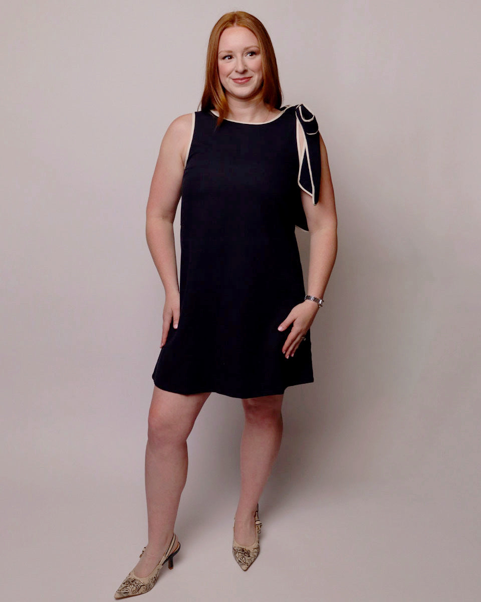 Woman wearing a navy dress with white accents against a plain background. Front view