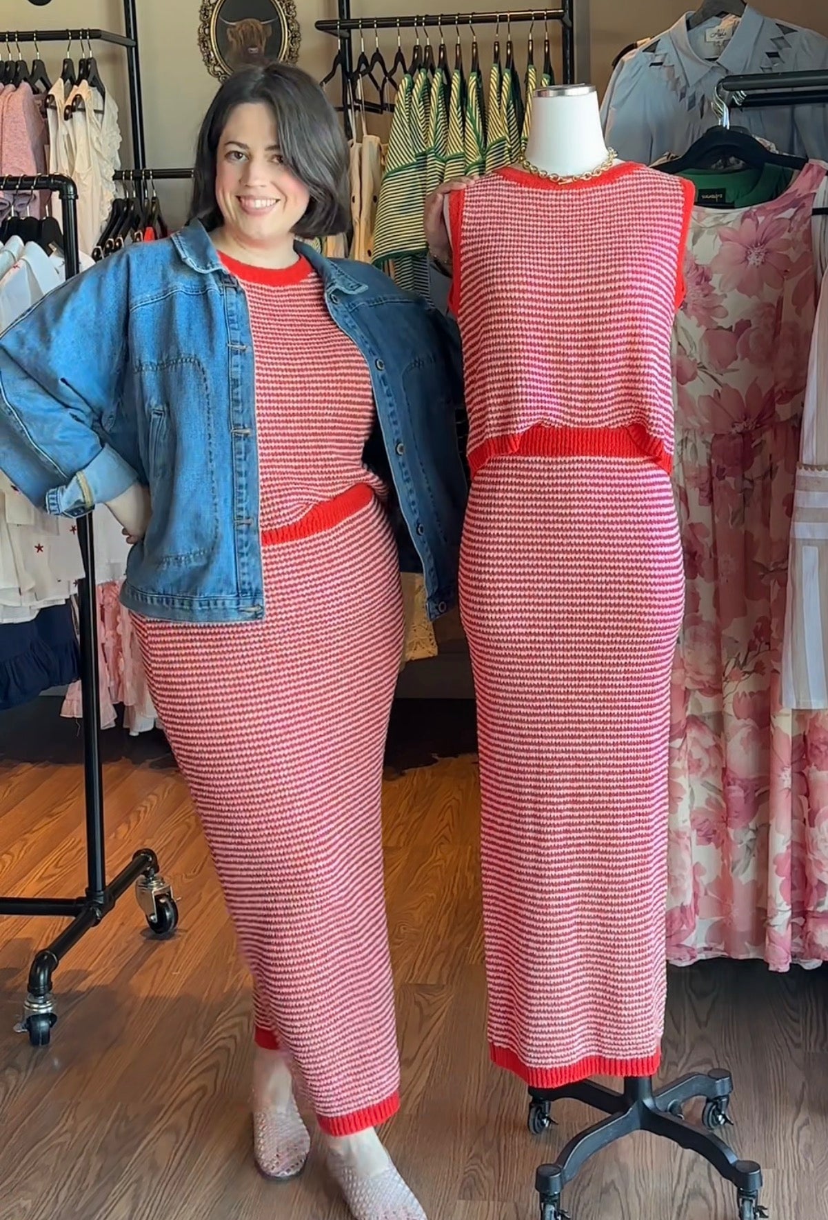 Woman wearing a red and white striped sweater skirt set with a denim jacket, standing next to a mannequin in a similar outfit.