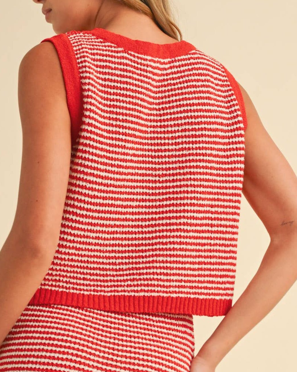Woman wearing a red and white striped sweater tank top on a neutral background