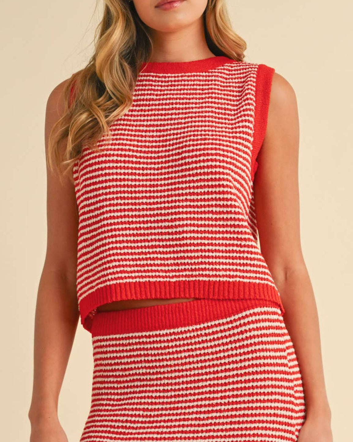 Woman wearing a red and white striped sweater tank top on a neutral background