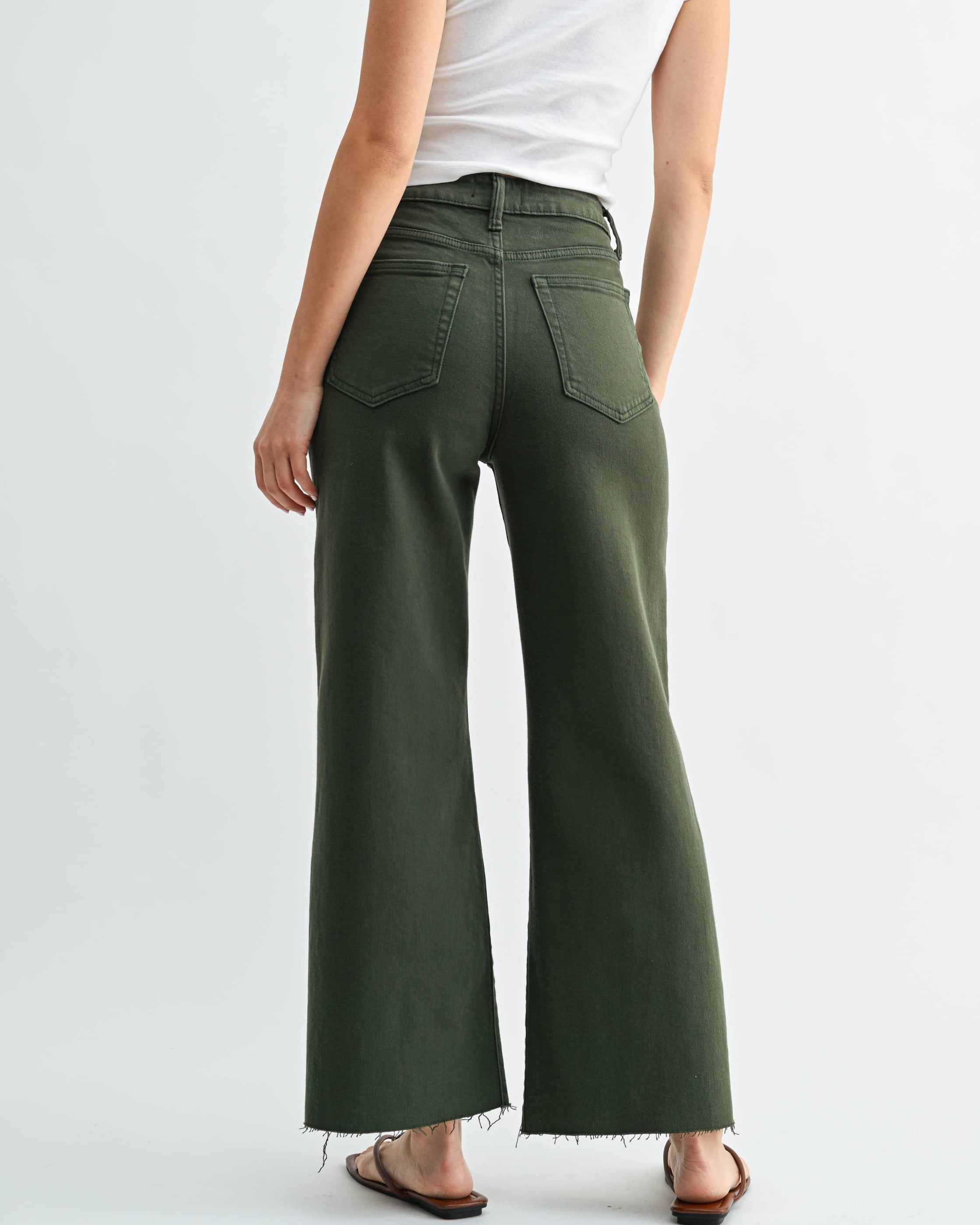 Woman wearing green wide-leg pants and a white top on a light gray background