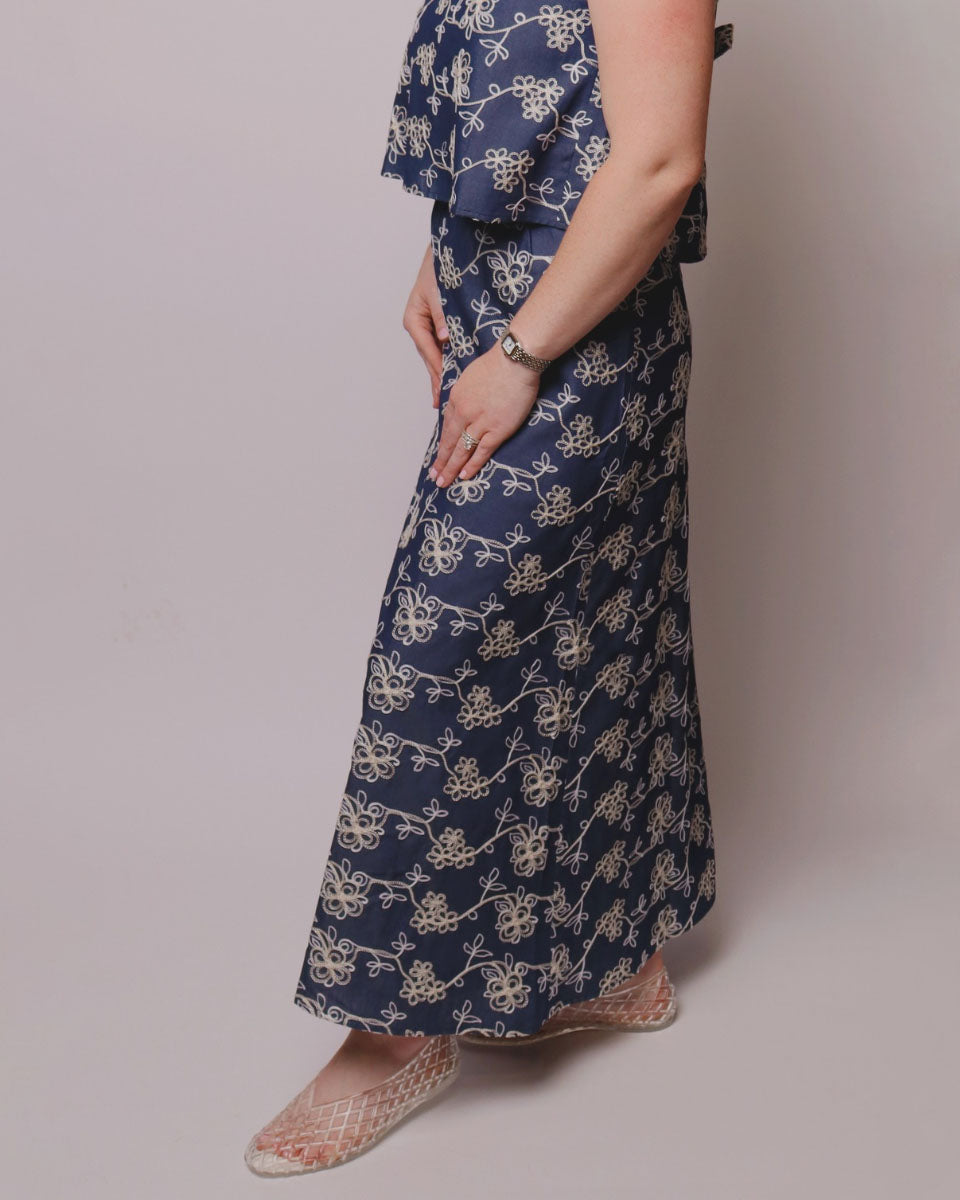 Person wearing a long blue floral patterned skirt on a plain background