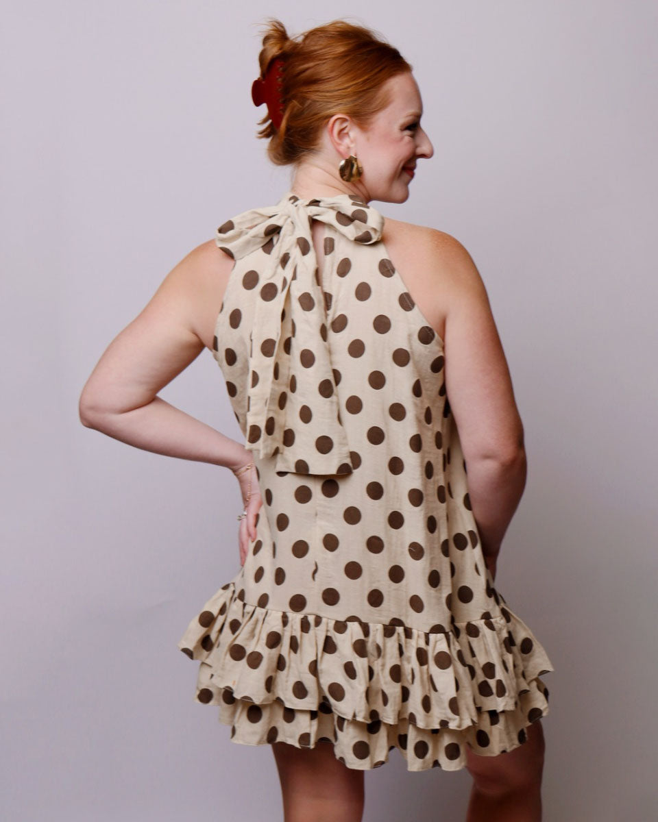 Woman wearing a beige dress with brown polka dots against a plain background