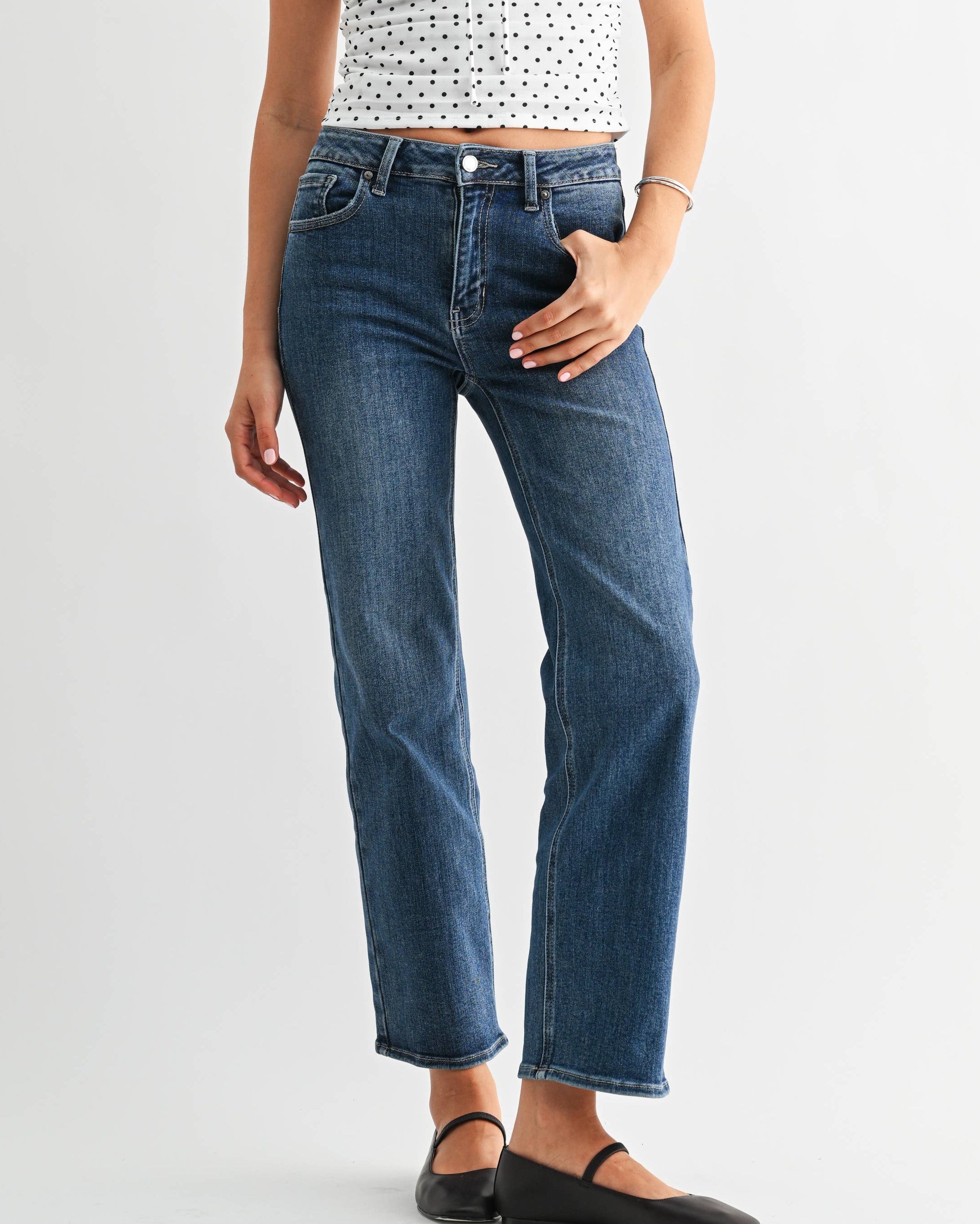 Woman wearing a polka dot top and blue jeans on a white background