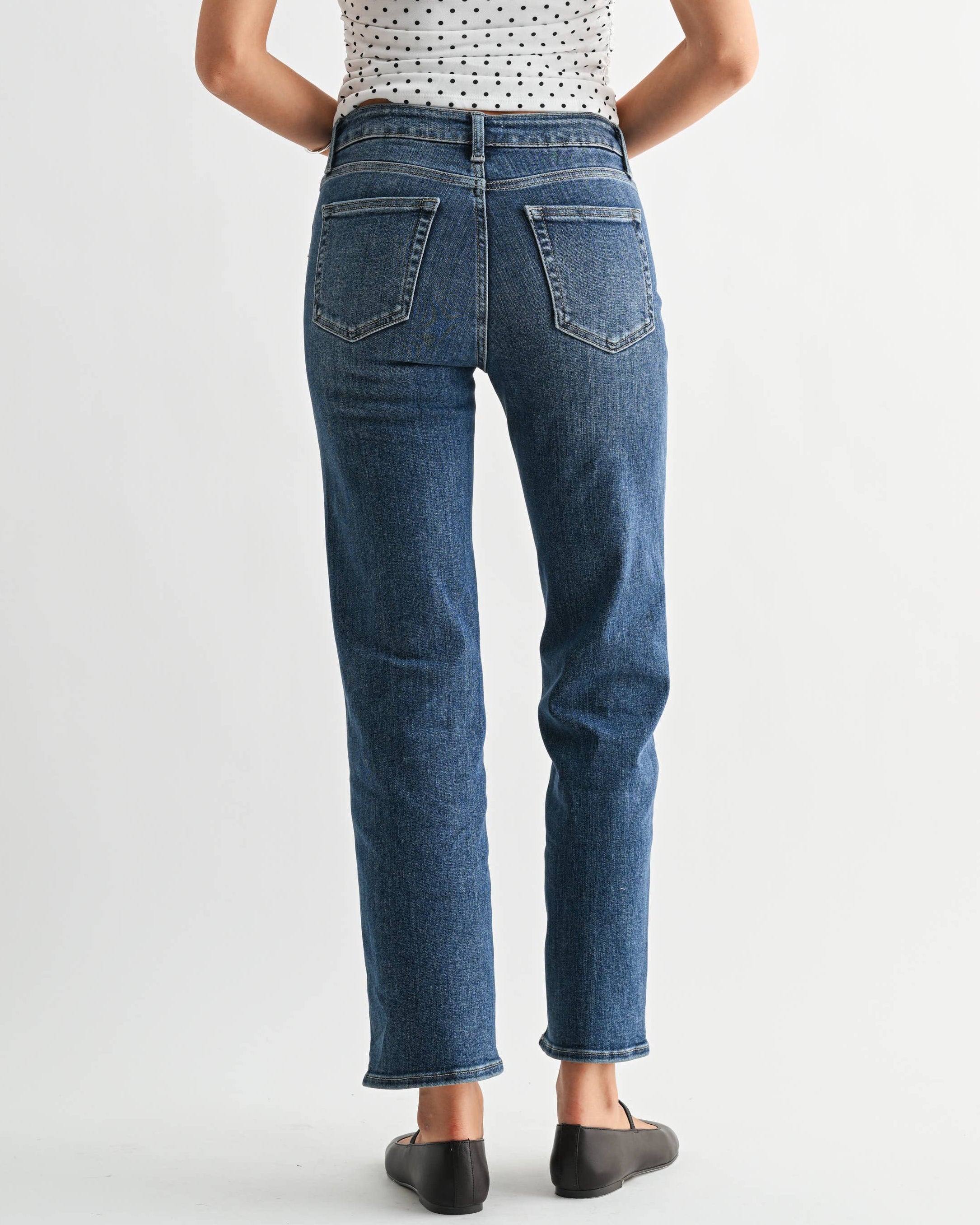 Woman wearing a patterned top and blue jeans on a white background
