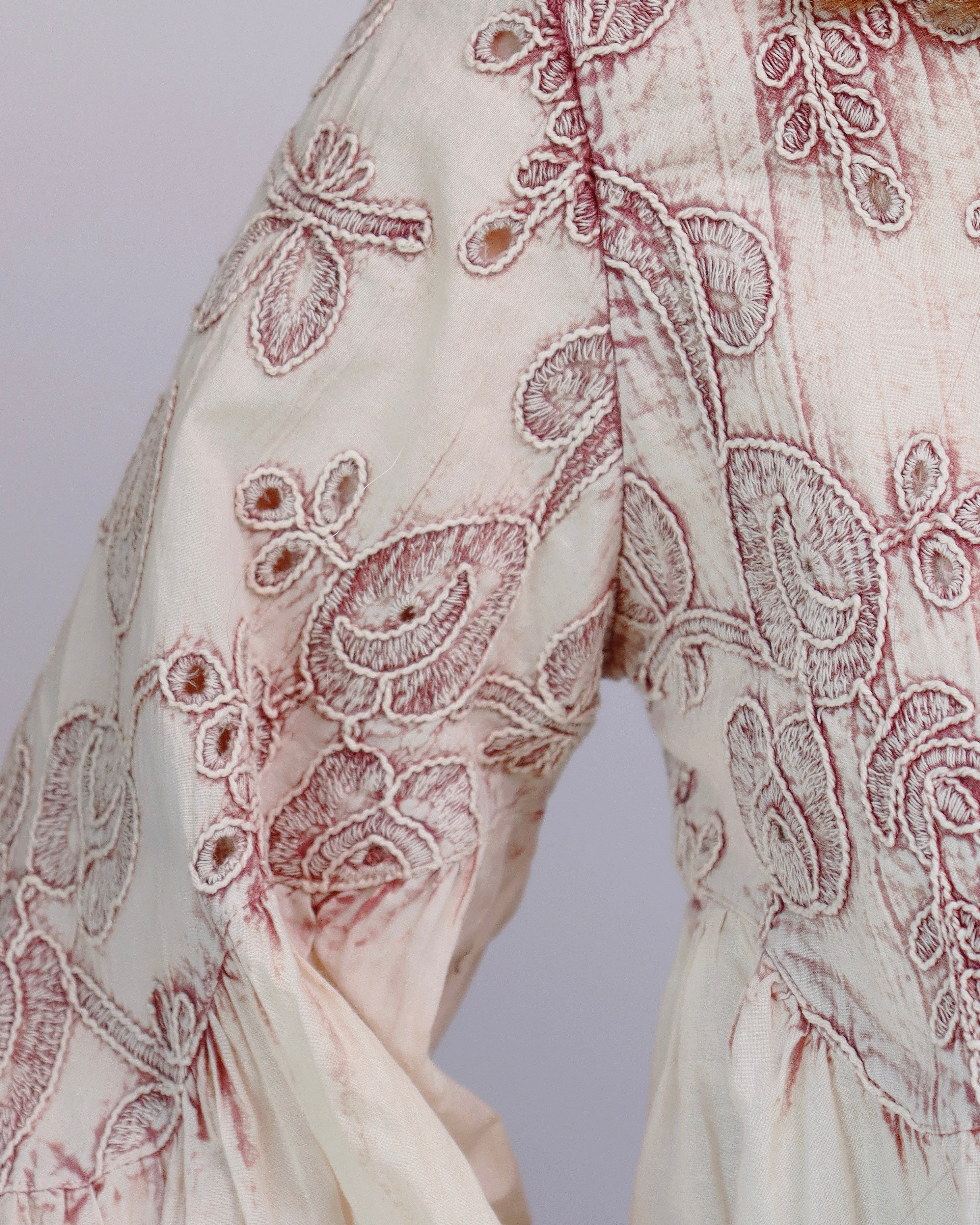 Close-up of a cream-colored fabric garment with intricate dusty rose embroidery and floral detailing.