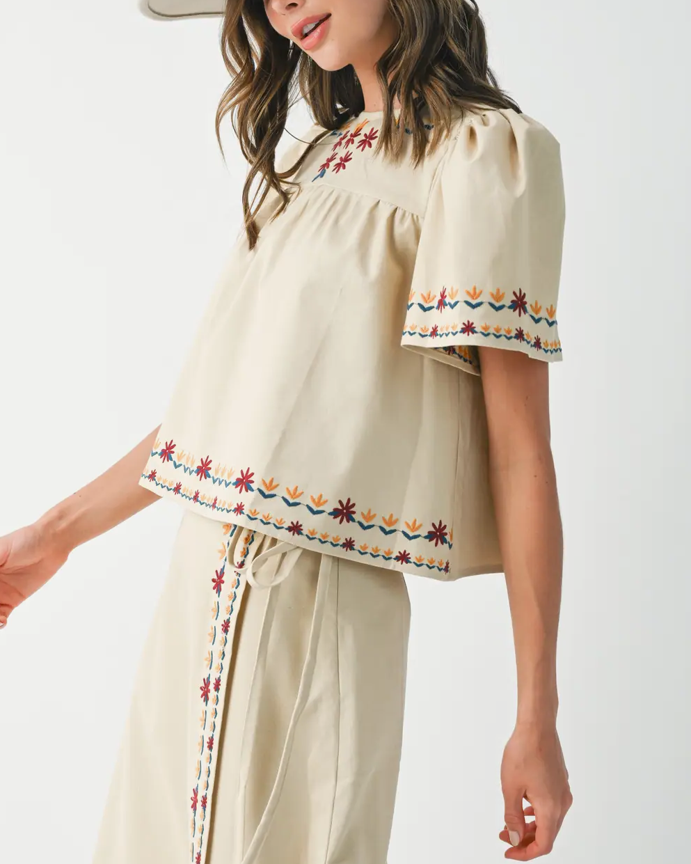 Woman wearing a cream-colored outfit with embroidered details on a white background