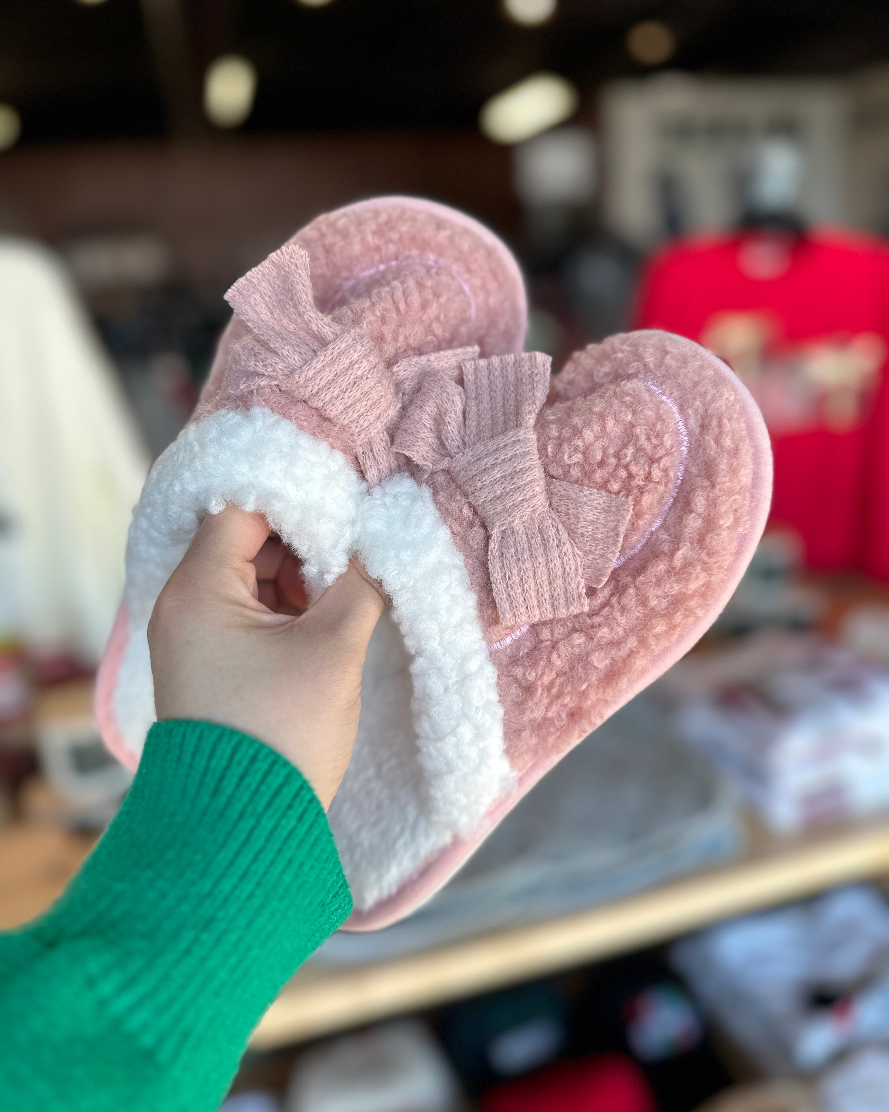 Pink slippers with white fur lining held by a person wearing a green sleeve.
