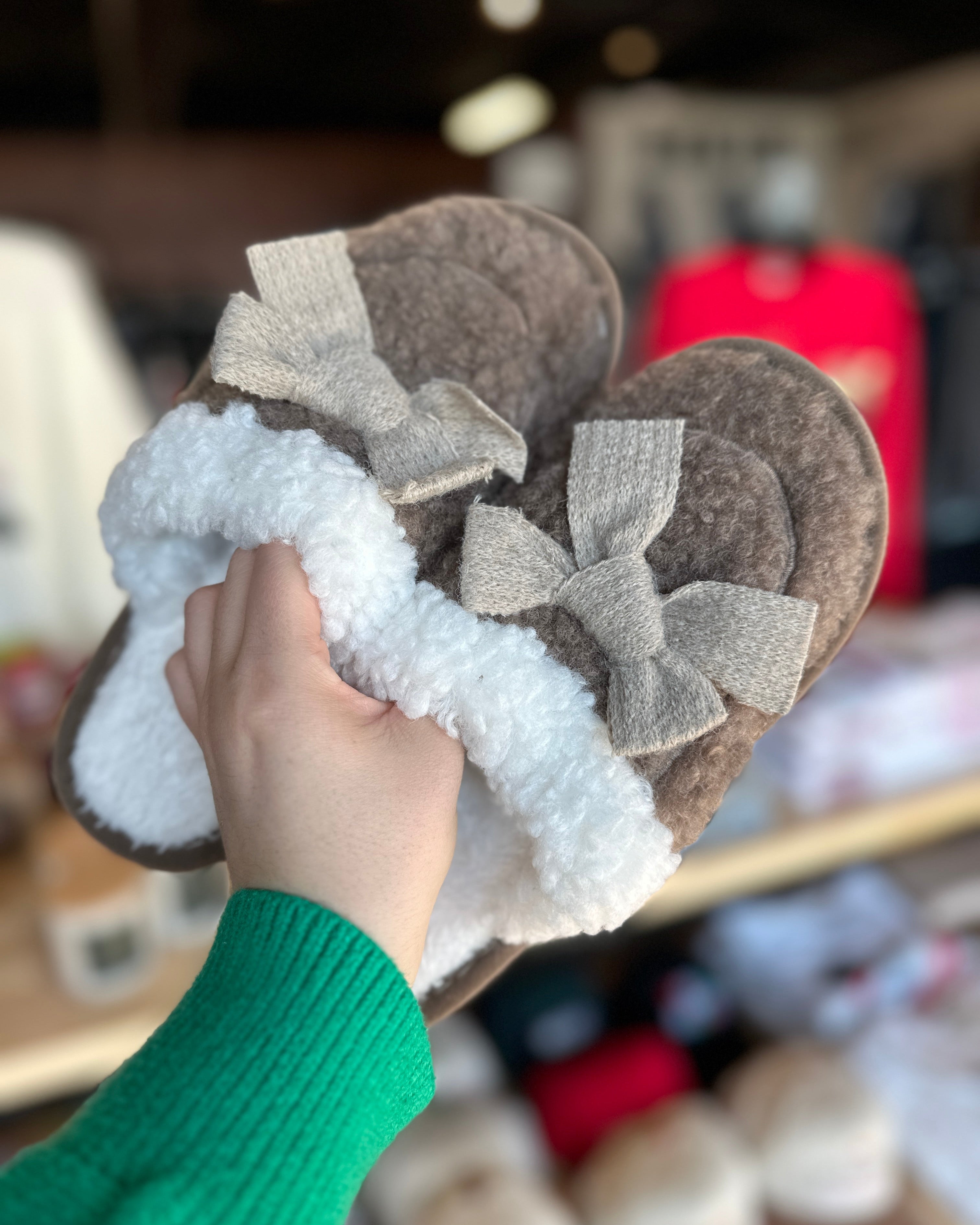 Brown slippers with white fuzzy sole held by a hand in a store setting