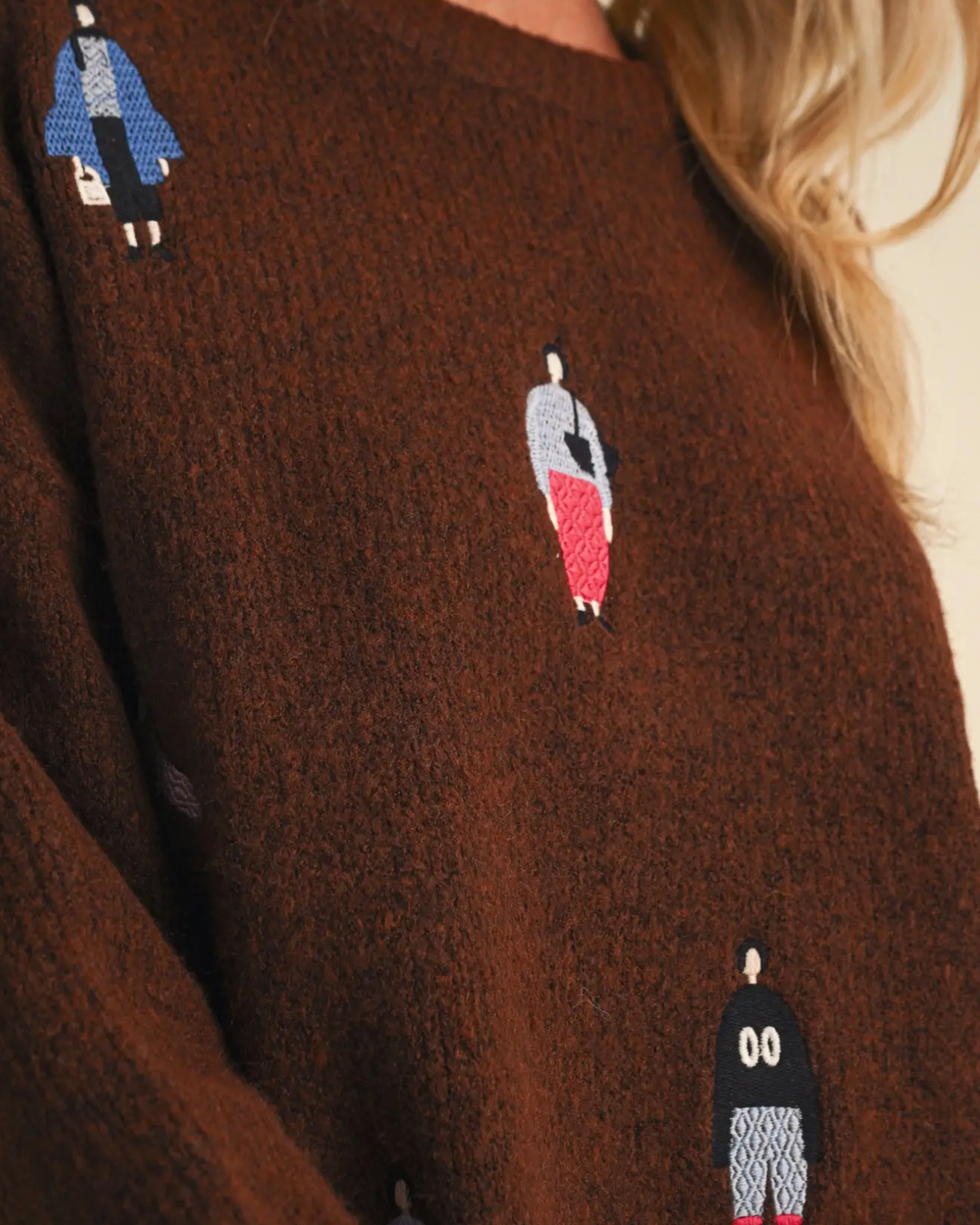 A close-up of a brown fuzzy knit sweater featuring embroidered penguin characters in blue, red, black, and white.