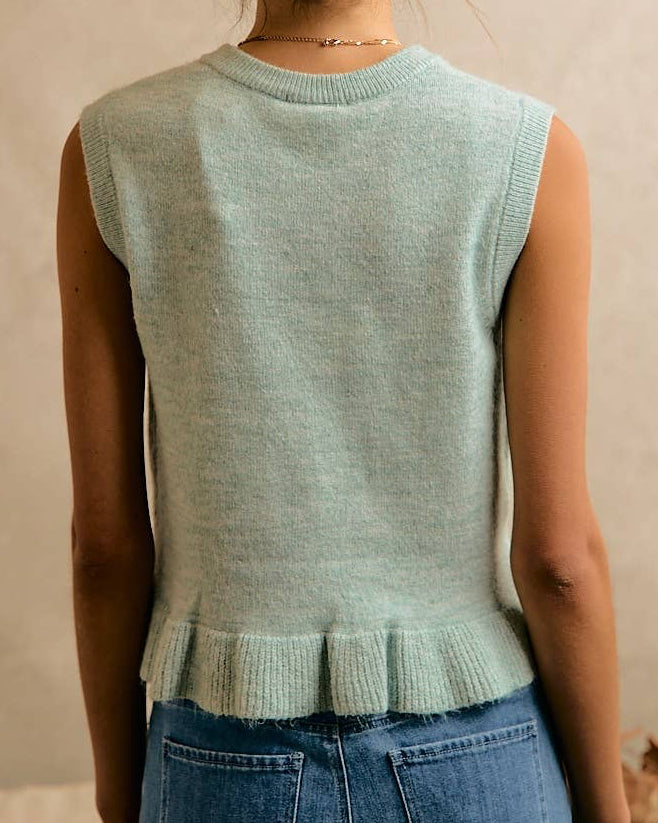 Person wearing a light green sleeveless top with a peplum waist against a beige background
