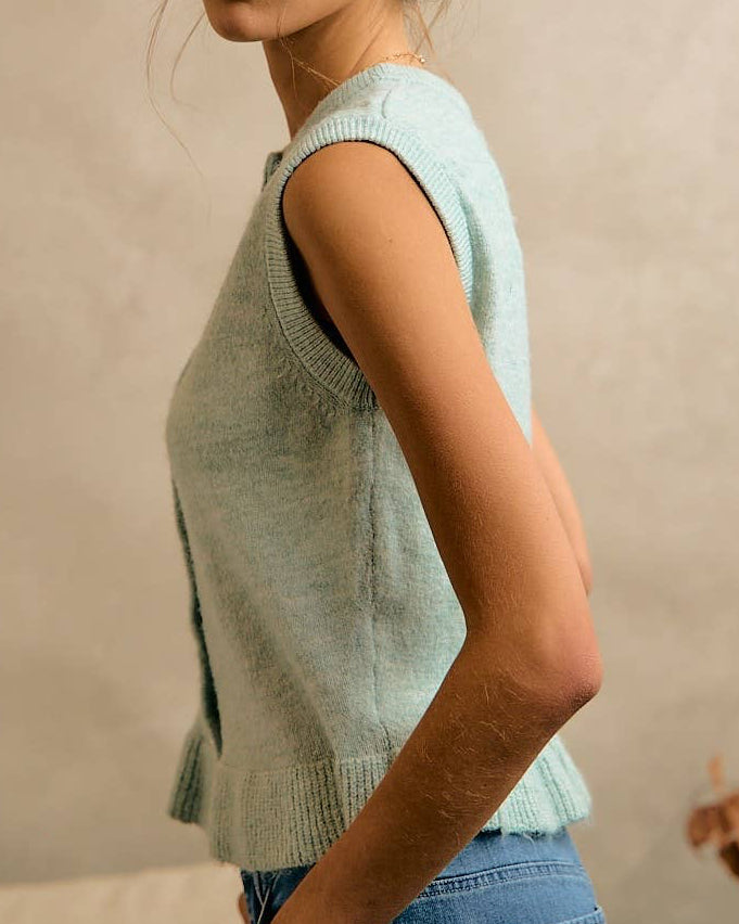 Woman wearing a light blue sleeveless sweater against a neutral background