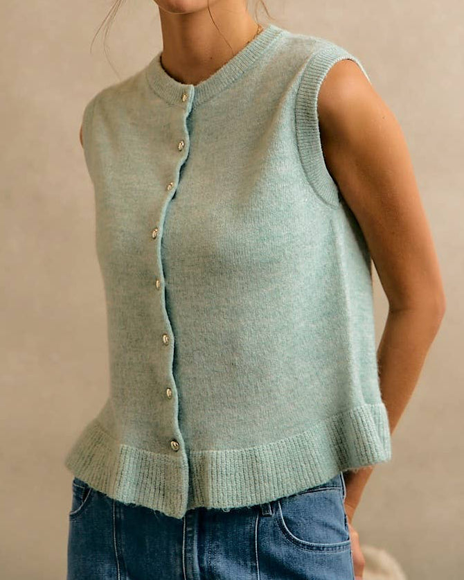 Woman wearing a light blue sleeveless knitted cardigan against a beige background