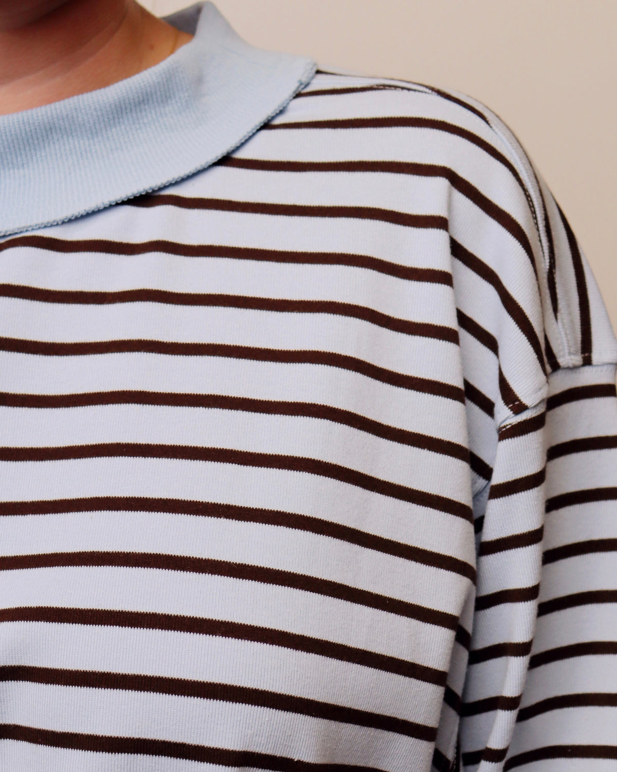 Close-up of a person wearing a white long-sleeve top with thin dark brown horizontal stripes and a light blue ribbed collar.
