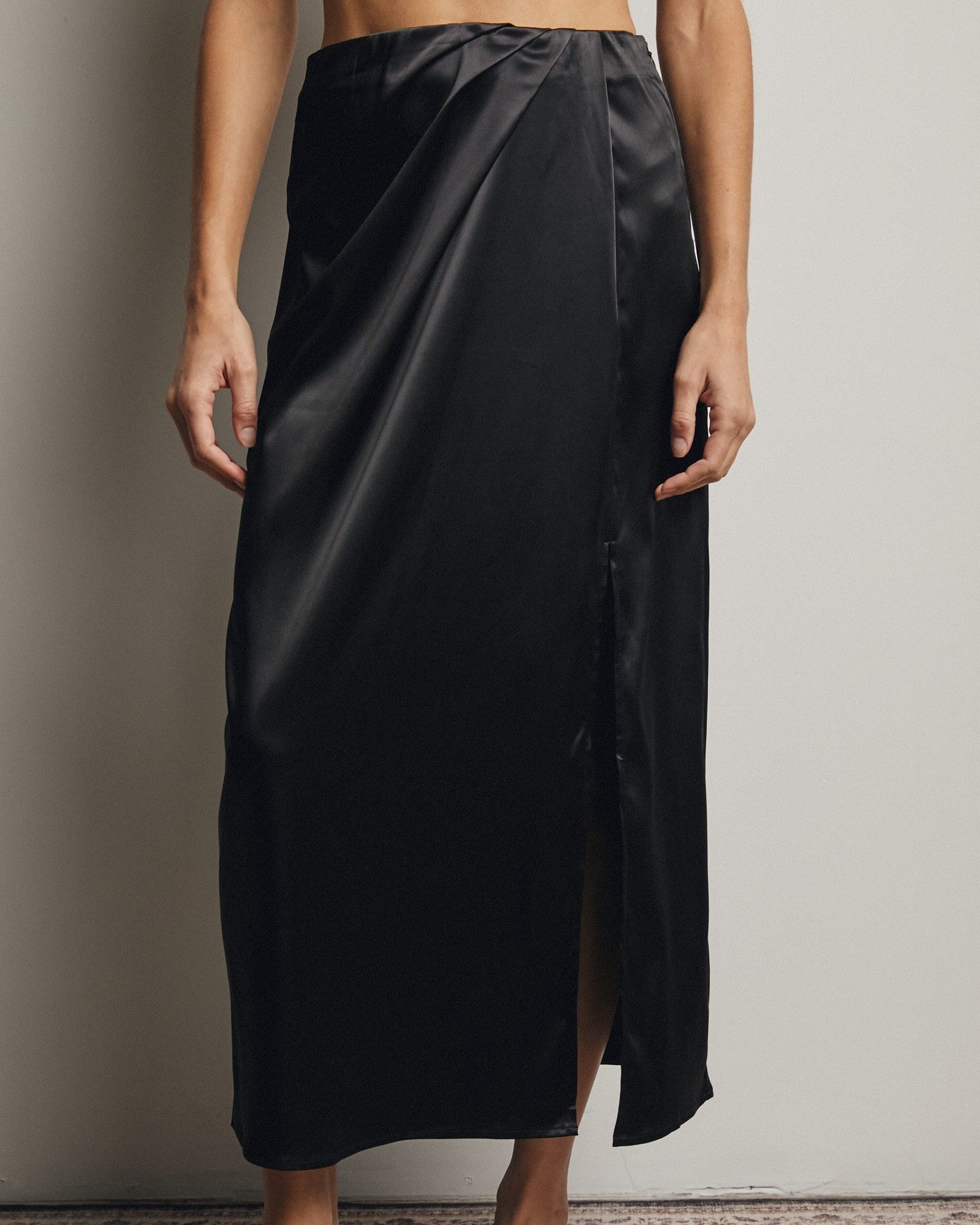 Person wearing a black satin skirt with a plain background