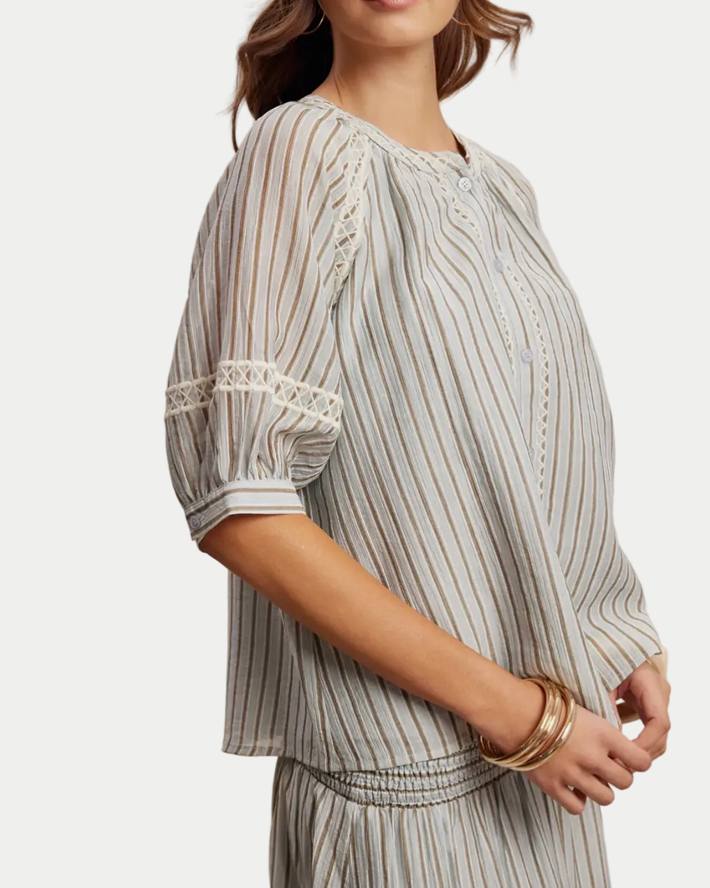 Woman wearing a light blue striped top on a beige background side view