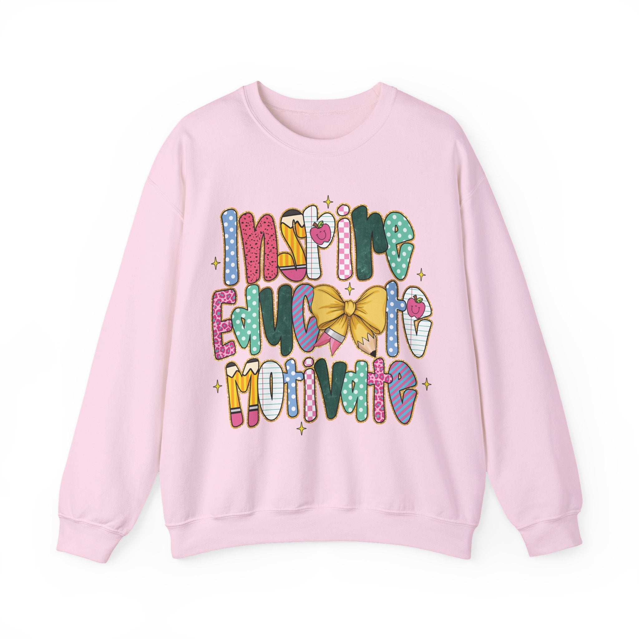 A light pink crewneck sweatshirt featuring a colorful graphic text design that reads 'INSPIRE EDUCATE MOTIVATE' in a playful, patterned font with a yellow bow and small stars.