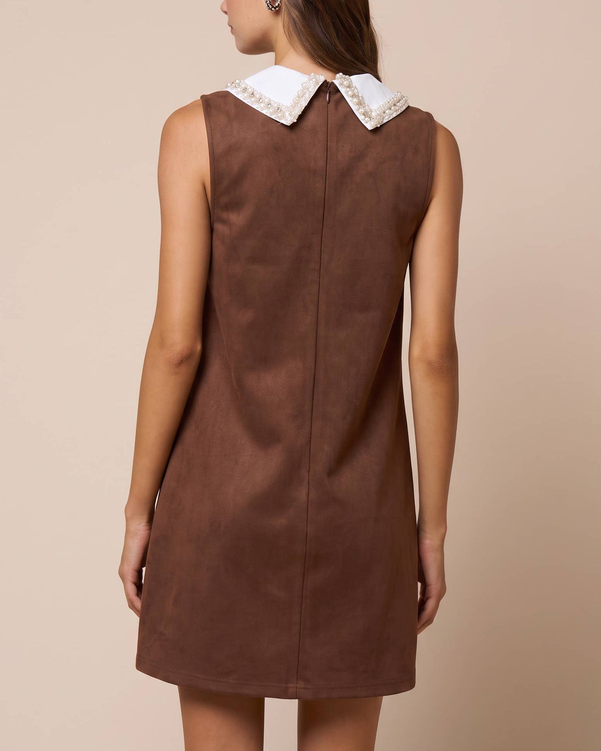 A woman shown from the back wearing a sleeveless brown dress with a contrasting white collar featuring delicate gold embroidery, set against a solid beige studio background. Isabella Rhinestone Contrast Collar Faux Suede Mini Shift Dress | Blackbird Boutique