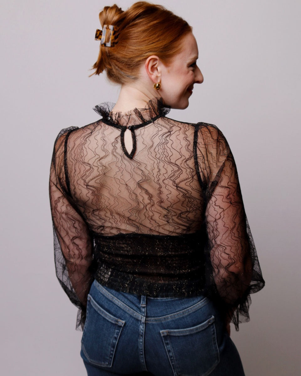 Woman wearing a black lace top and blue jeans against a plain background