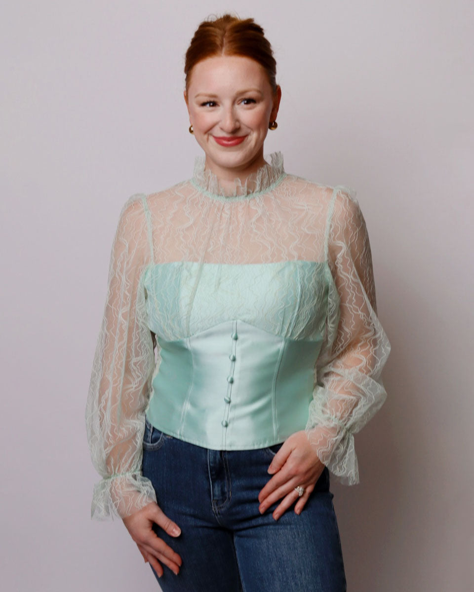 Woman wearing a light green corset top with sheer sleeves against a plain background