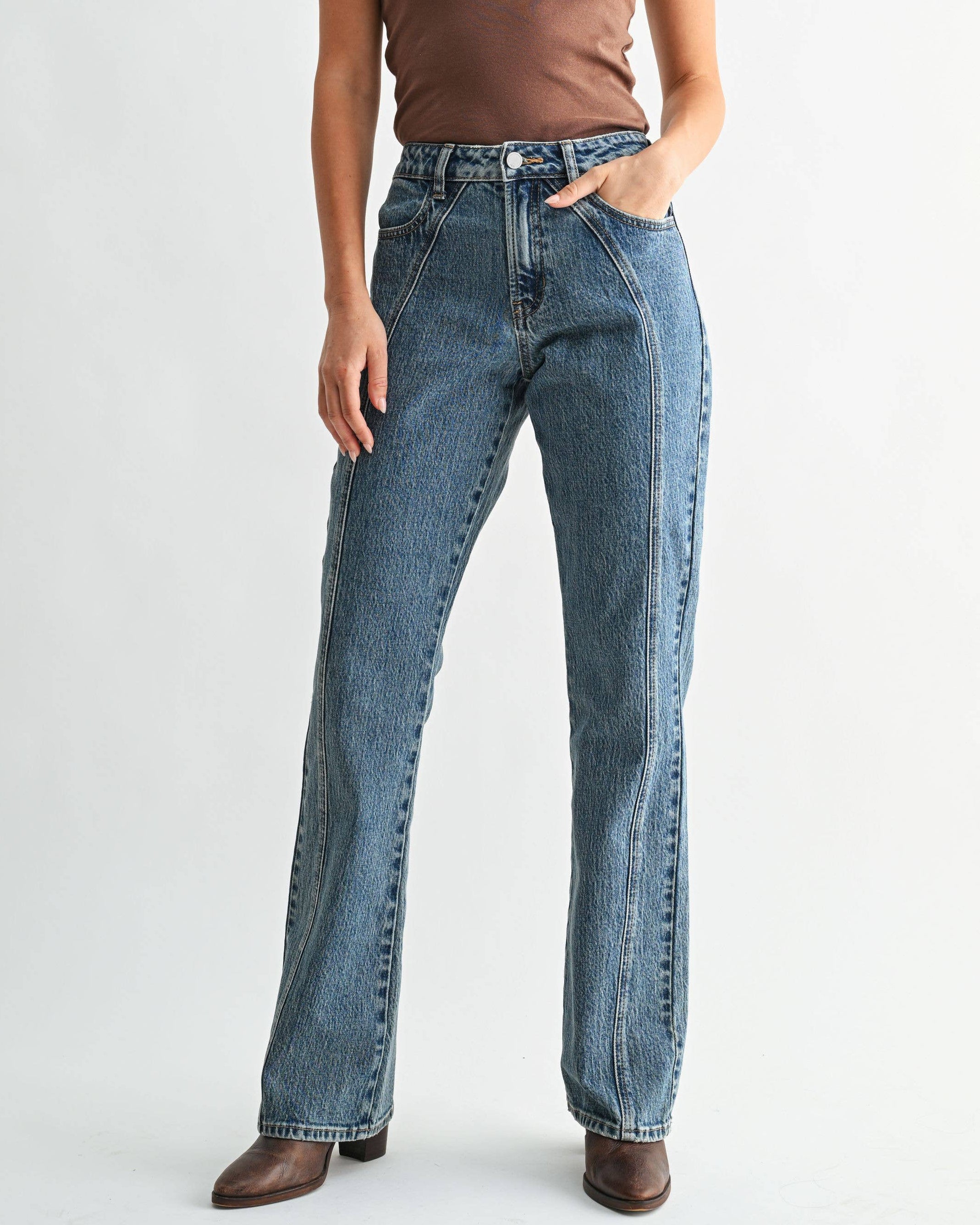 A woman modeling a brown short-sleeve t-shirt and high-waisted, wide-leg blue jeans against a plain light gray studio background.