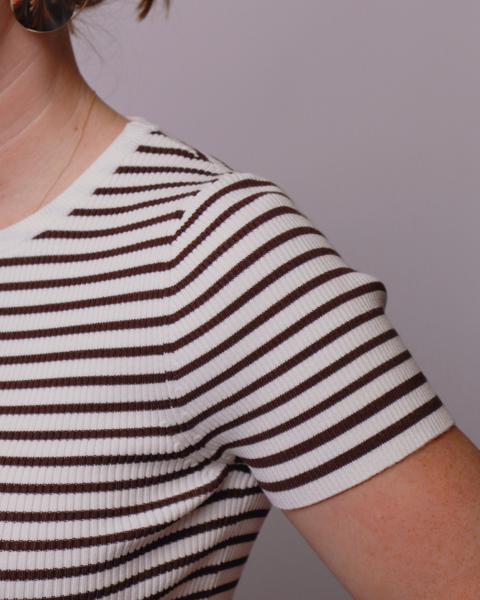 Close-up of a person wearing a white and brown striped shirt against a plain background