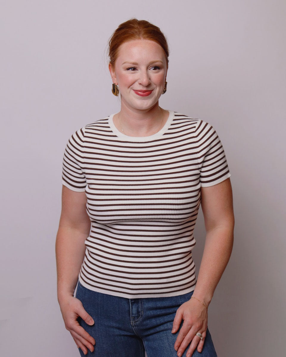 Woman wearing a striped shirt and jeans against a plain background