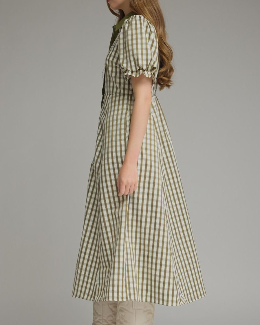 Woman wearing a green checkered dress with beige boots on a plain background