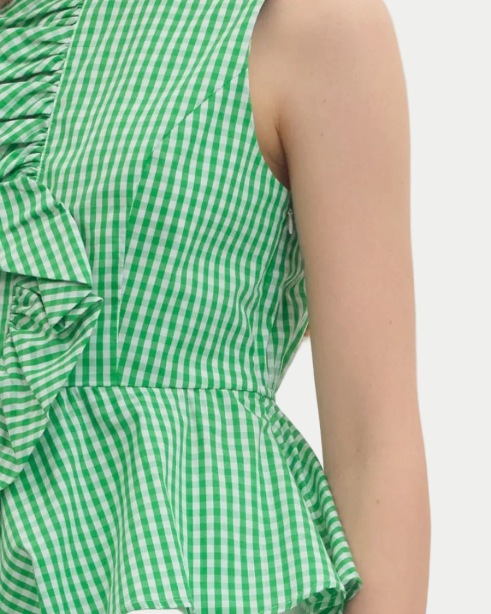 Woman wearing a green checkered peplum top and white shorts on a plain background.  unique sleeveles top.  Summer top.  Vacation Top.  Weekend wear.