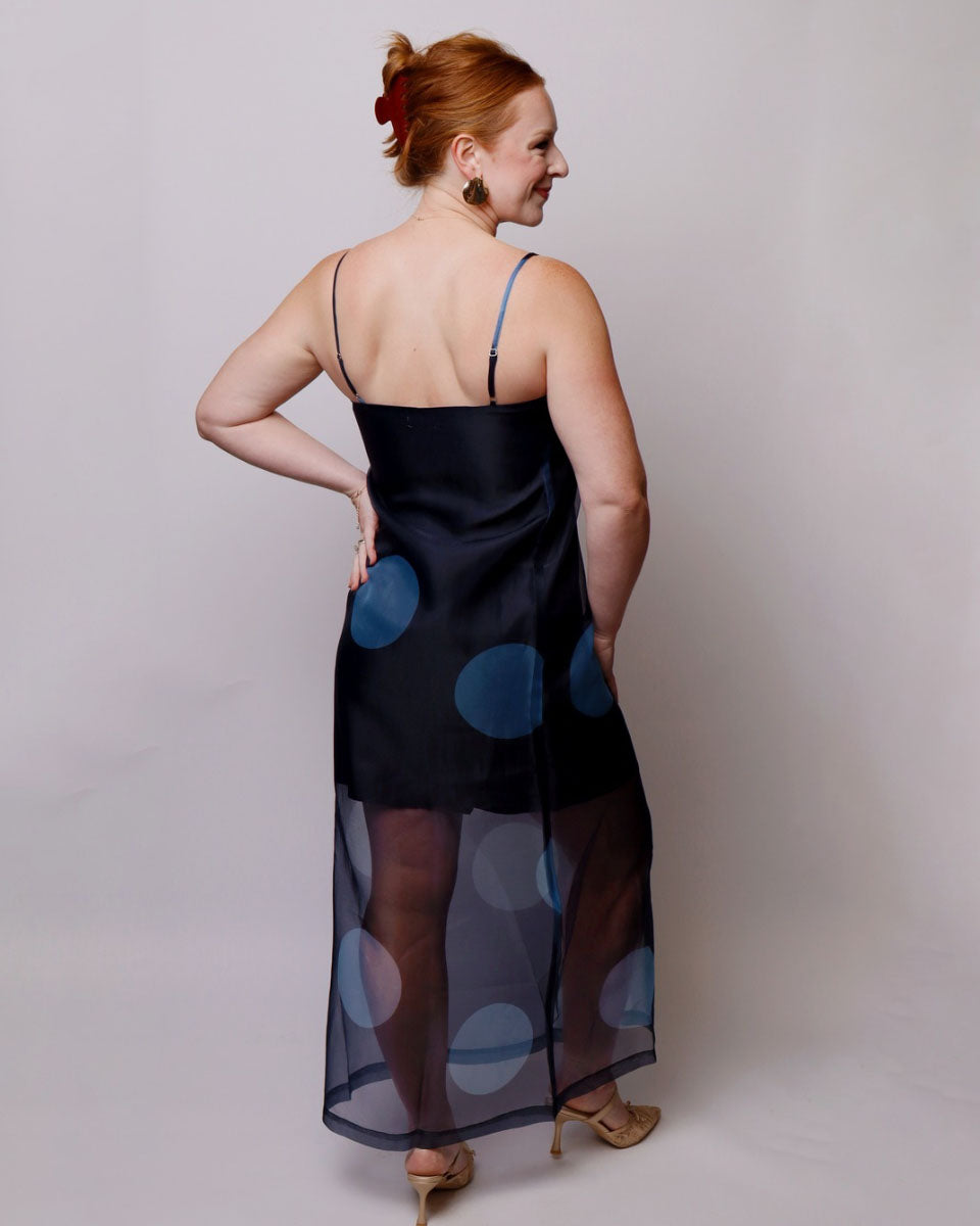 Woman wearing a black dress with blue polka dots on a plain background