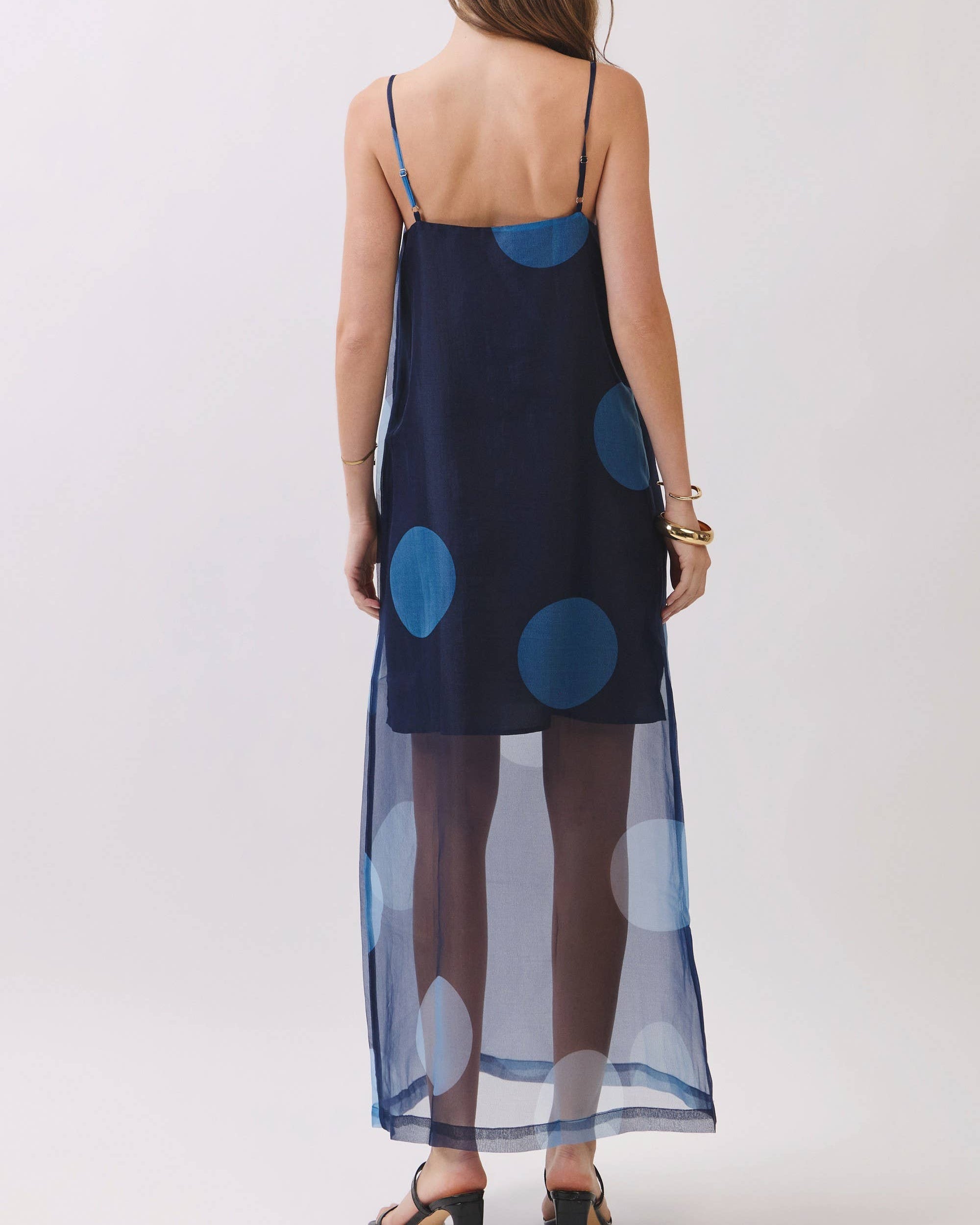 Model wearing a navy mini dress with blue polka dots maxio overlay on a neutral background . back view