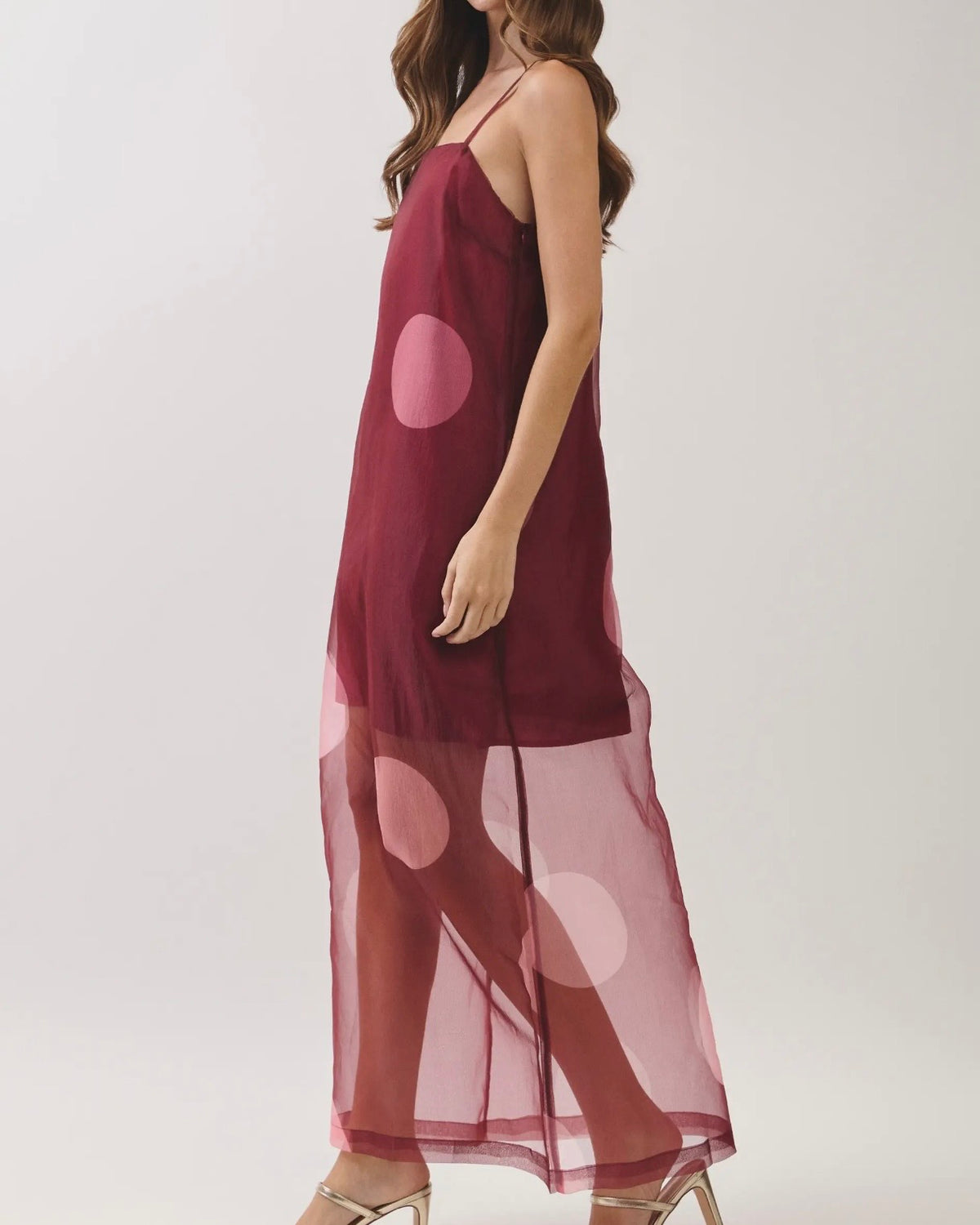Model wearing a burgundy dress with a sheer overlay with large polkadots on a neutral background