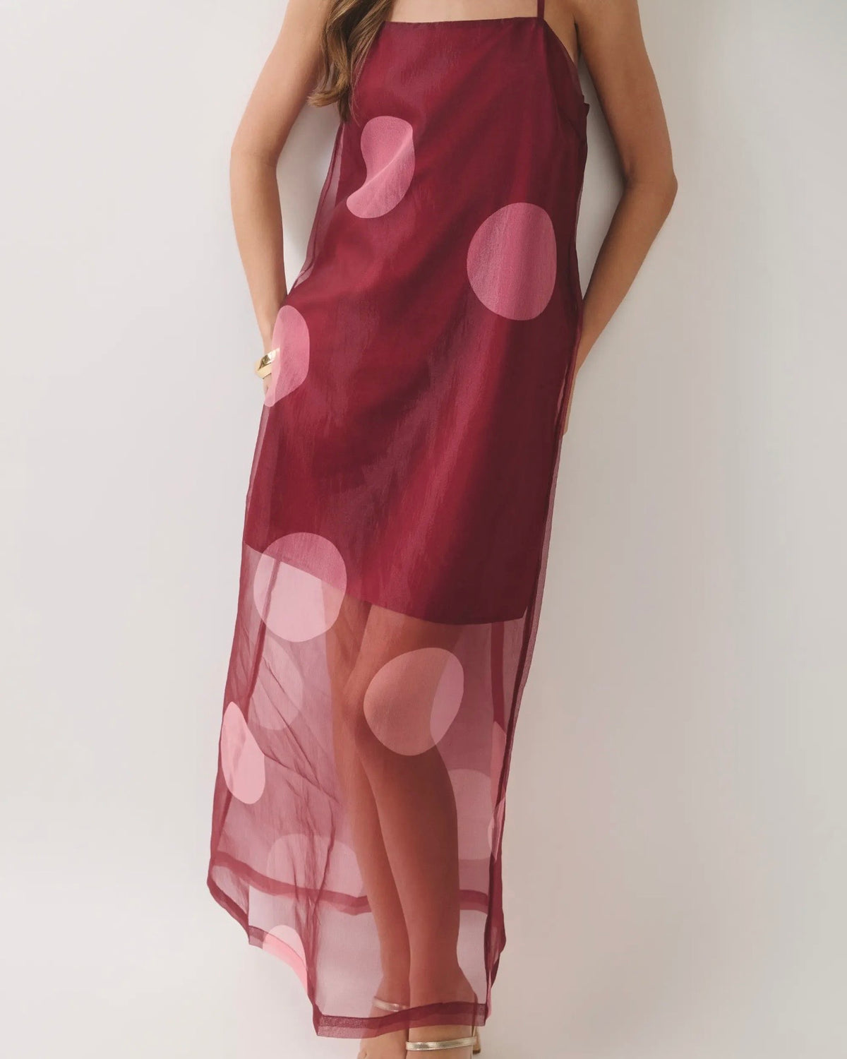Model wearing a burgundy dress with a sheer overlay with large polkadots on a neutral background