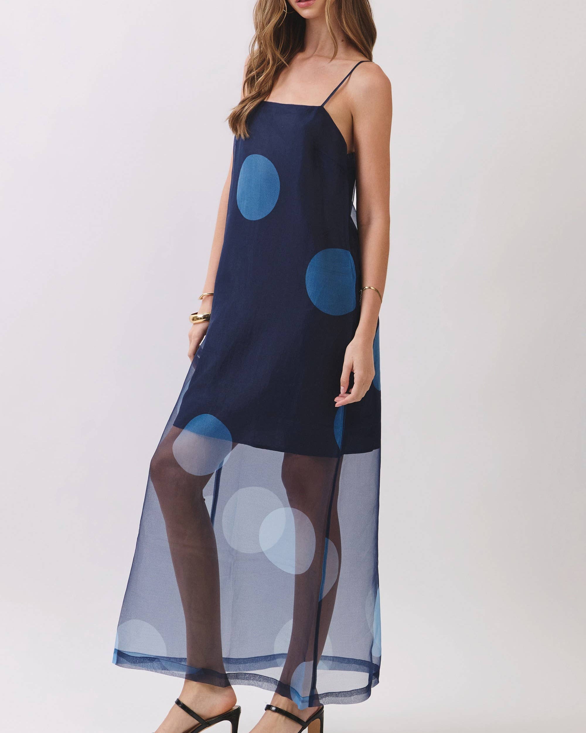 Model wearing a navy mini dress with blue polka dots maxio overlay on a neutral background . side view