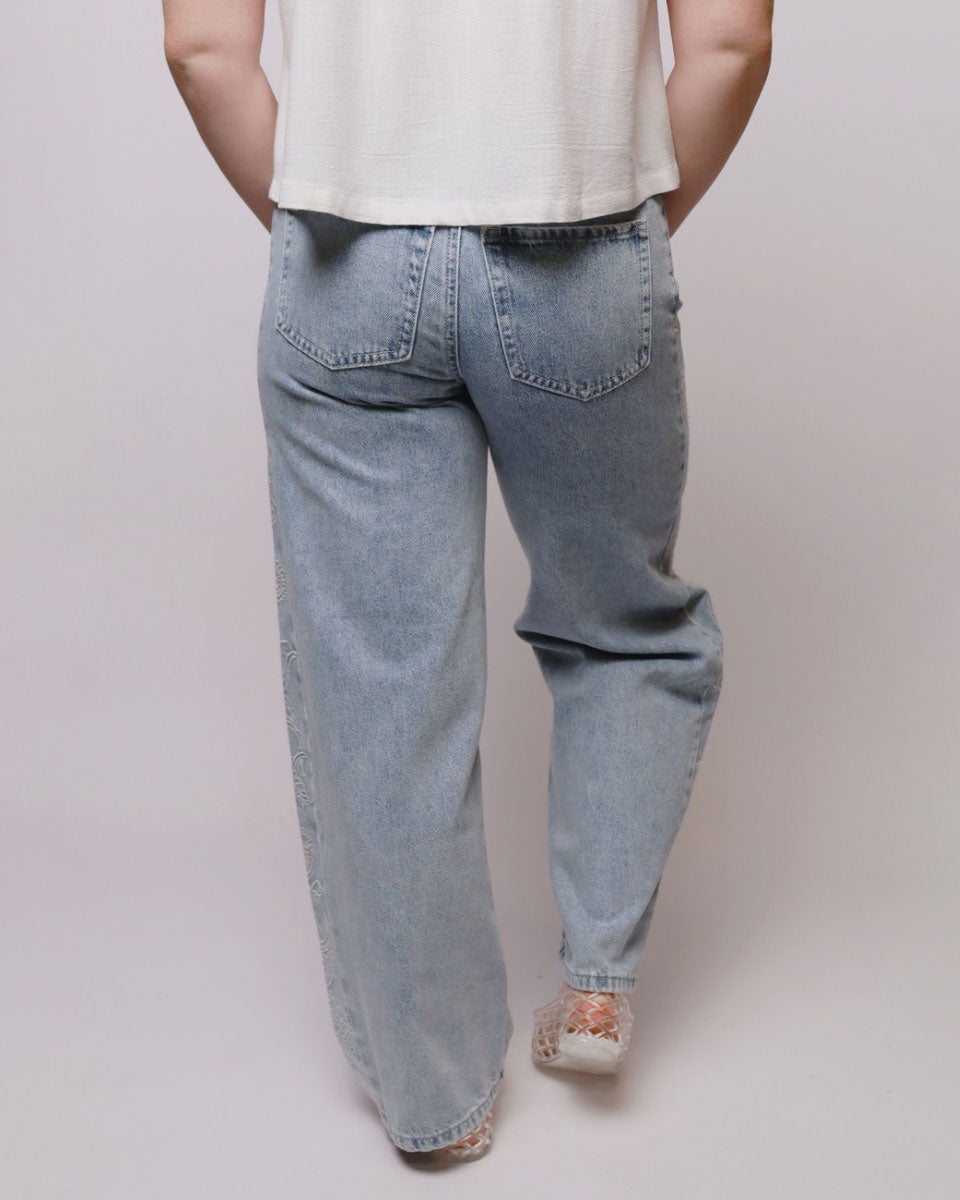 A person shown from the back wearing light-wash blue jeans, a white sleeveless top, and lace-up shoes against a plain light gray studio background.