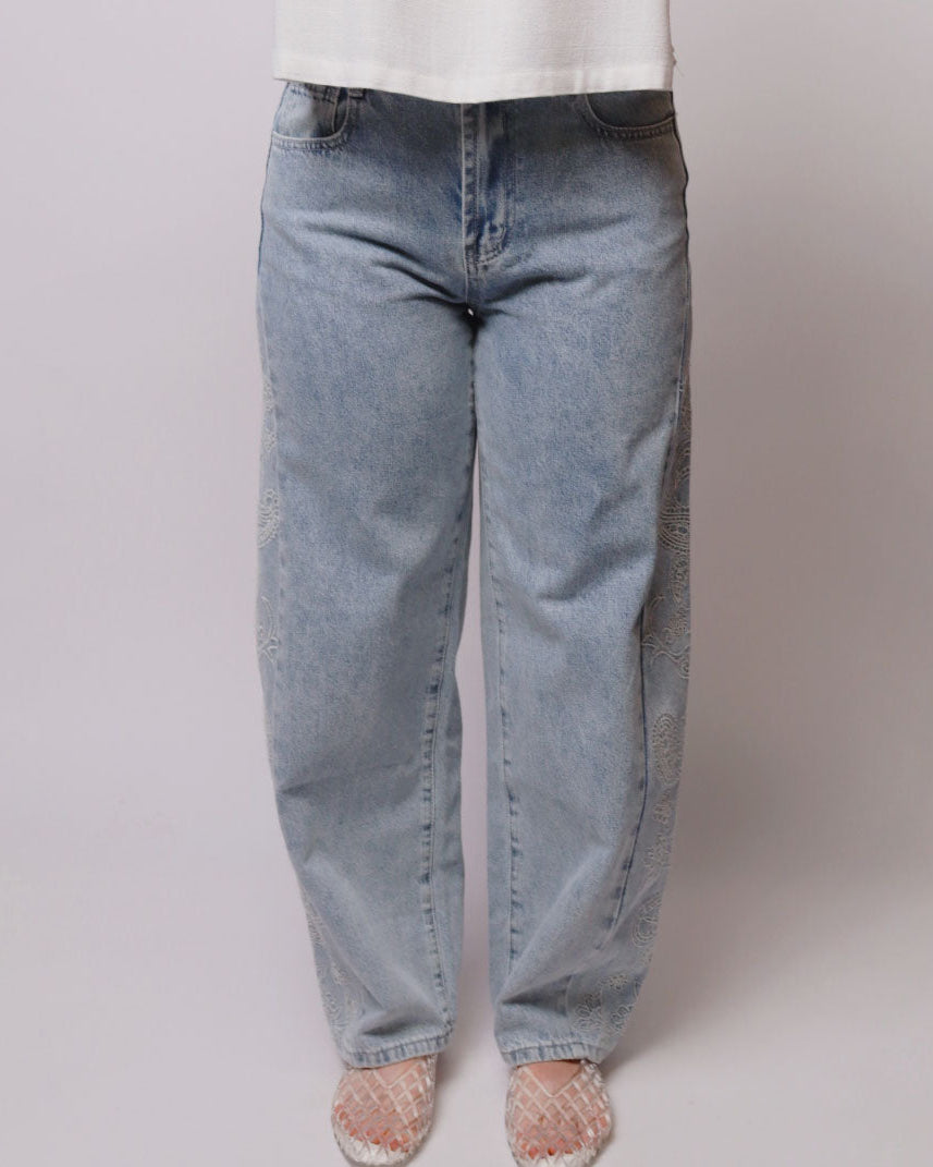 A person wearing light-wash blue straight-leg jeans, a white top, and pink lace-up sandals, standing against a plain light gray studio background.