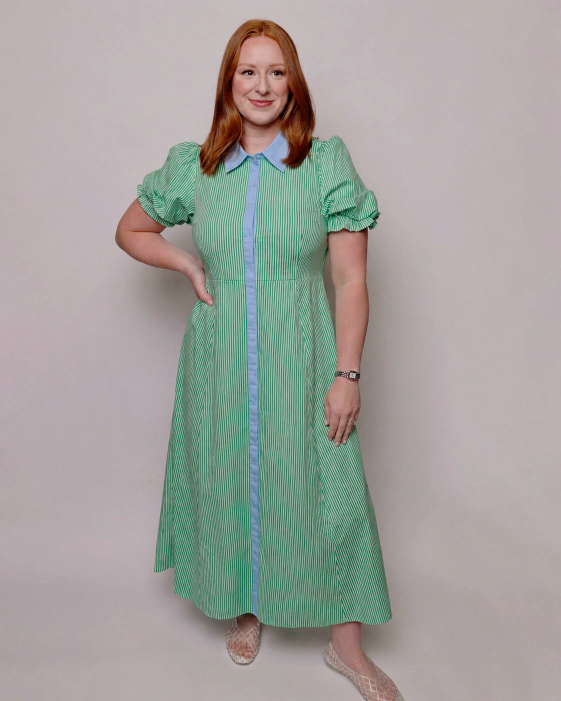 Woman wearing a green dress with a blue contrast on a plain background. Front view