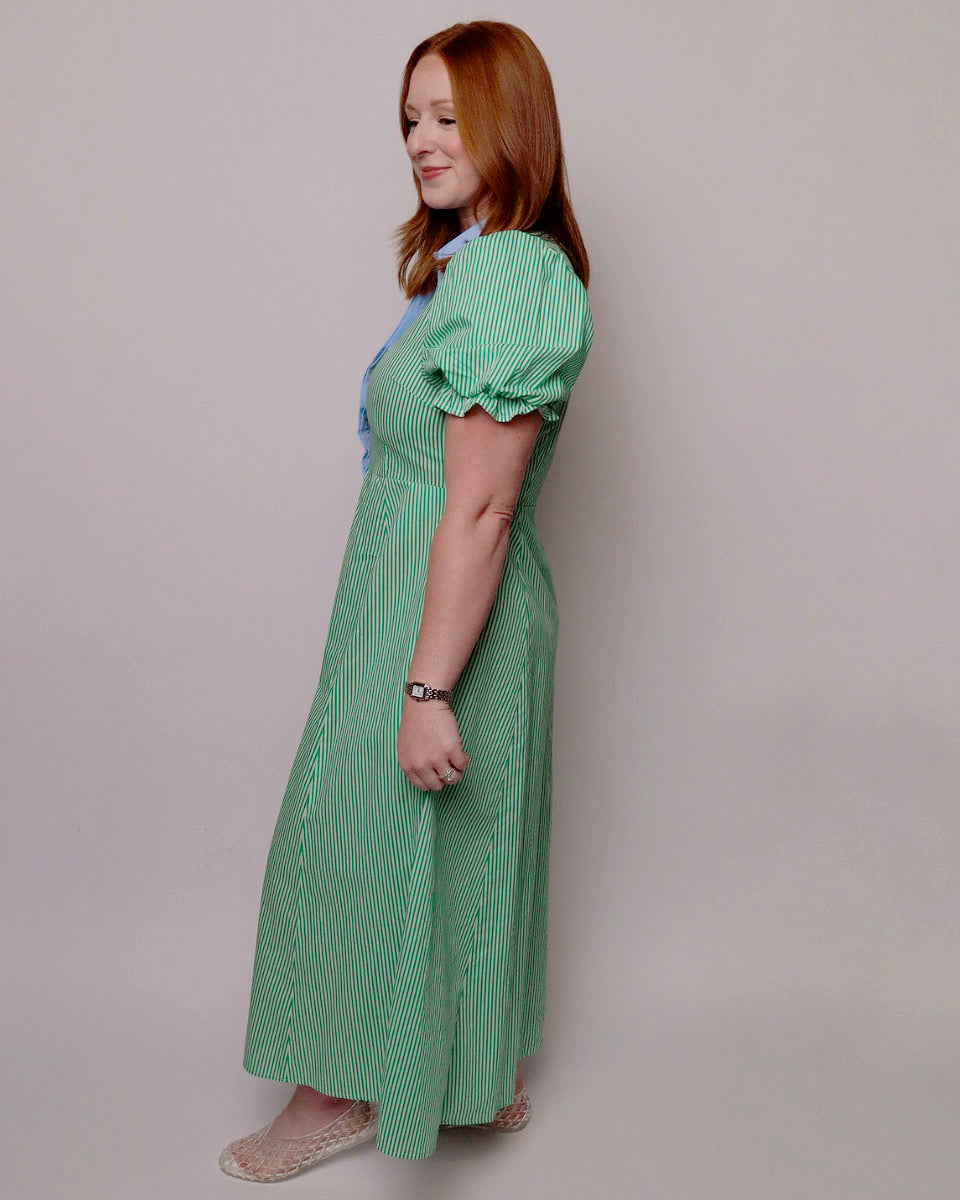 Woman wearing a green dress with puffed sleeves against a plain background. Side view