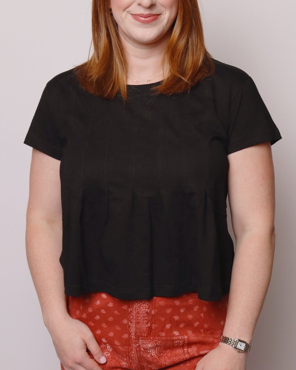 Person wearing a black top and red patterned pants against a plain background