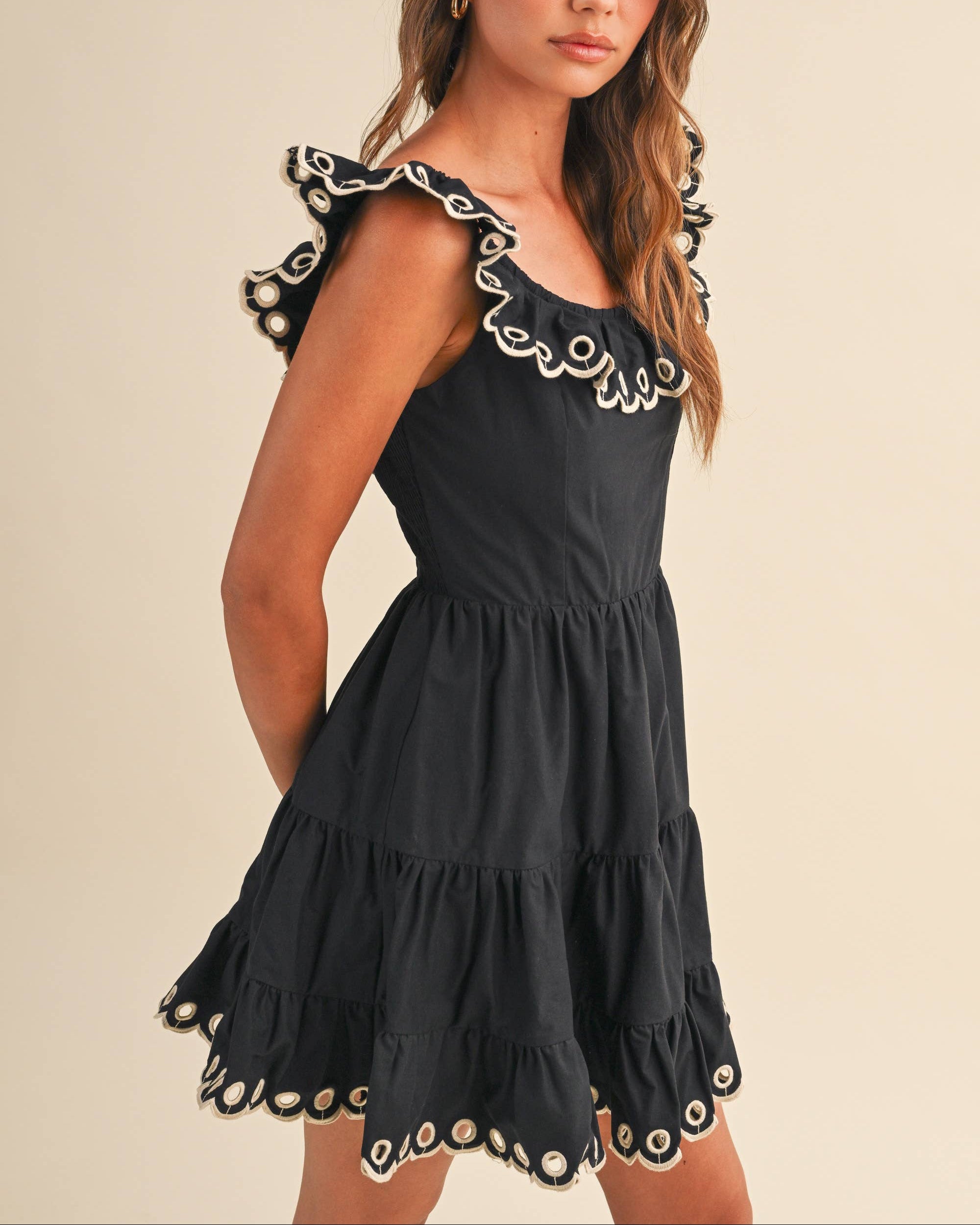 Woman wearing a black dress with Taupe embroidery on a neutral background side view