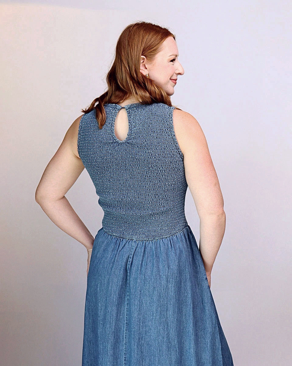 A woman wearing a sleeveless textured blue dress, shown from the back and side against a plain light gray studio background.